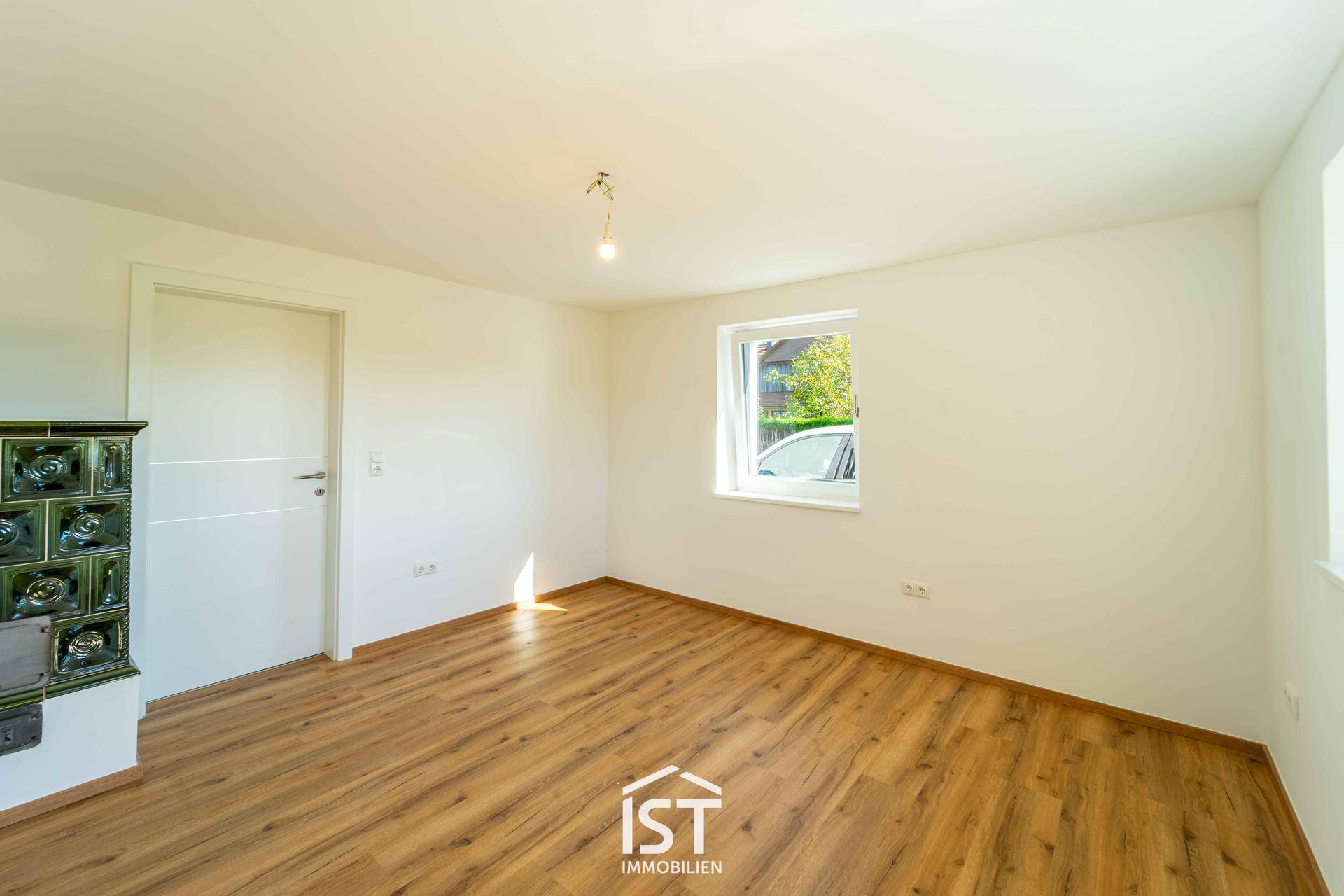 Gemütliches Zimmer mit Laminatboden und einem traditionellen Kachelofen an der Wand.