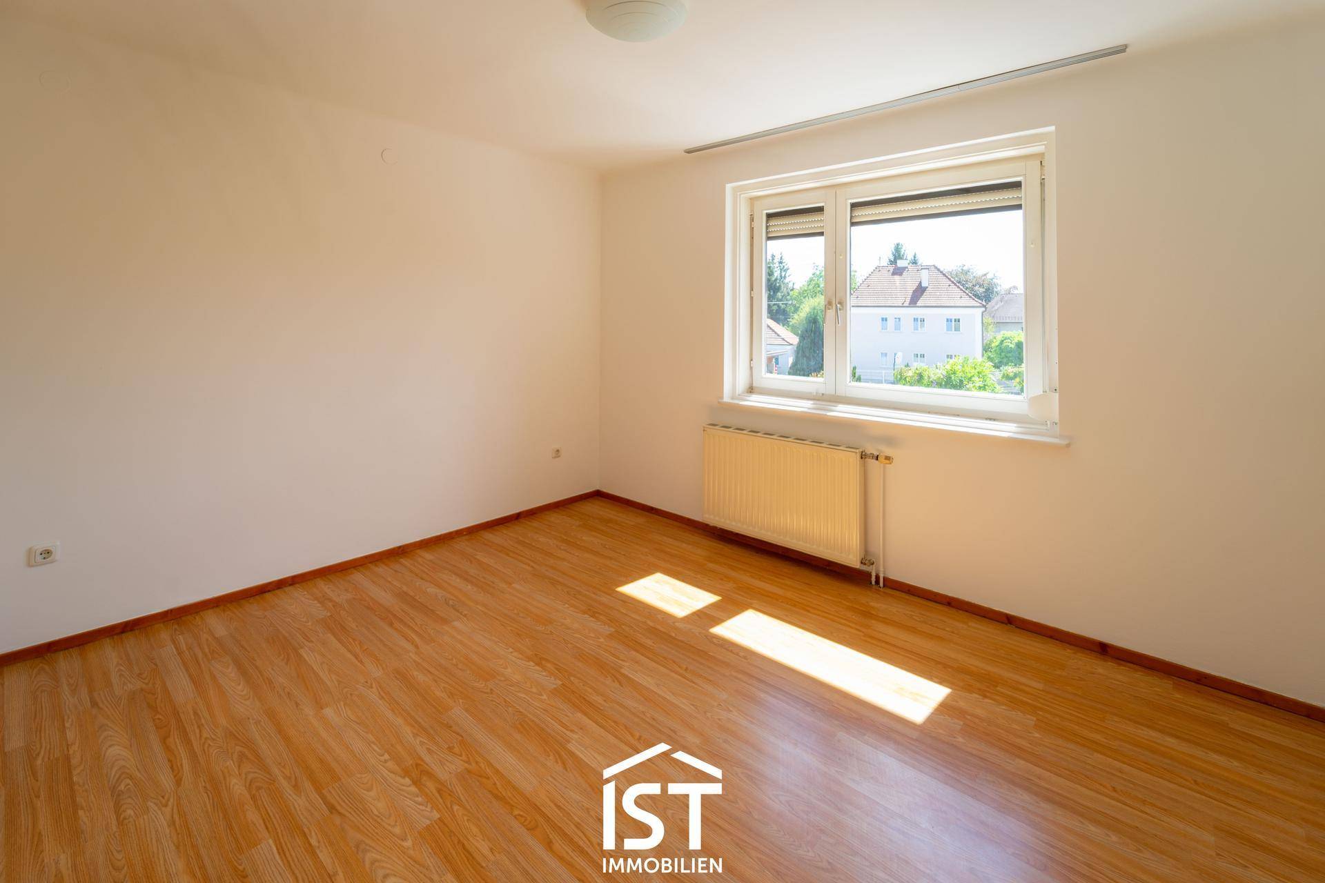 Helles Schlafzimmer mit Laminatboden, großem Fenster und viel natürlichem Lichteinfall.