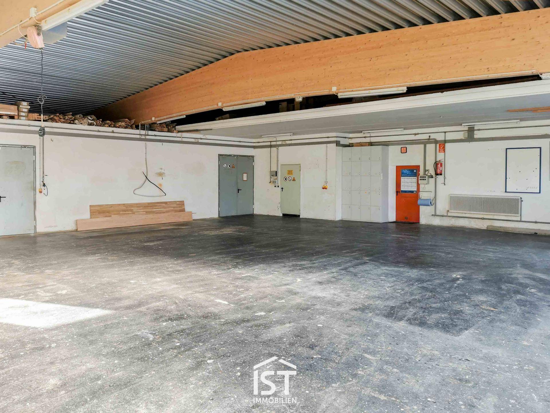 Geräumiger Lagerbereich mit hoher Decke, sichtbaren Holzträgern und robustem Betonboden. Verschiedene Türen sind zu sehen.