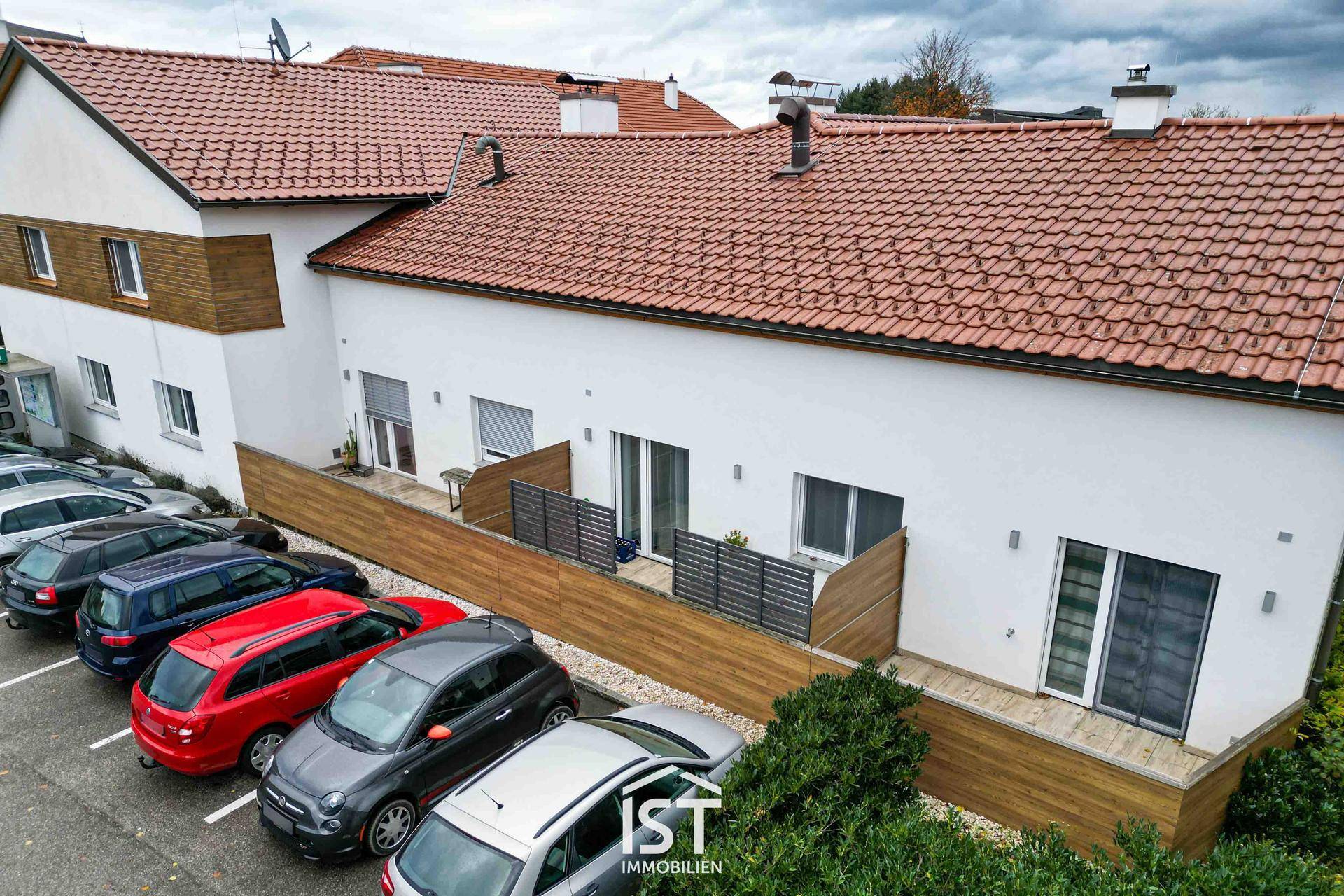 Rückansicht des Gebäudes mit Terrassen im Erdgeschoss und Parkplätzen.