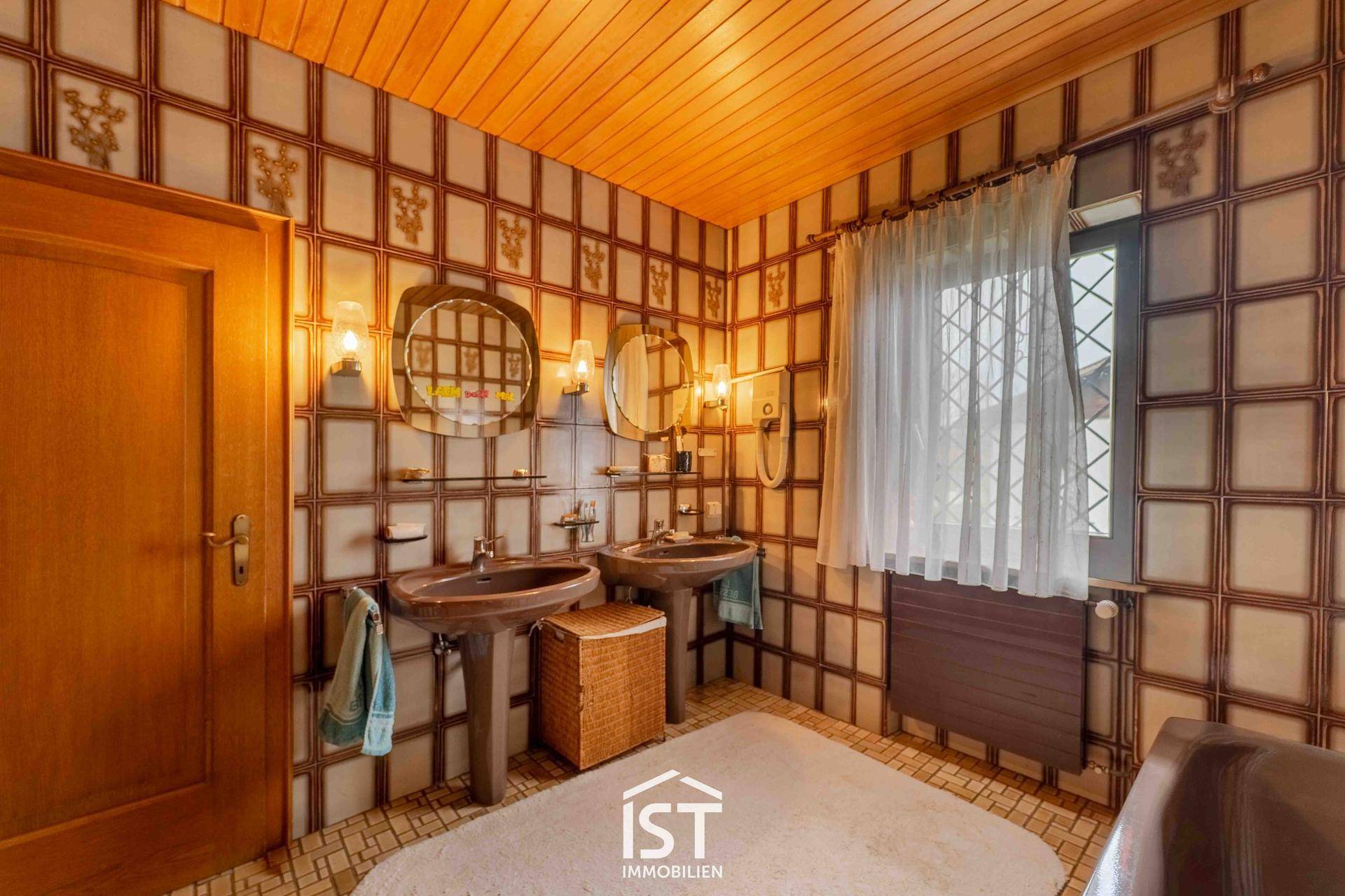 Badezimmer im 80er-Jahre-Stil mit Doppelwaschbecken, gemusterten Fliesen und Holzdecke.