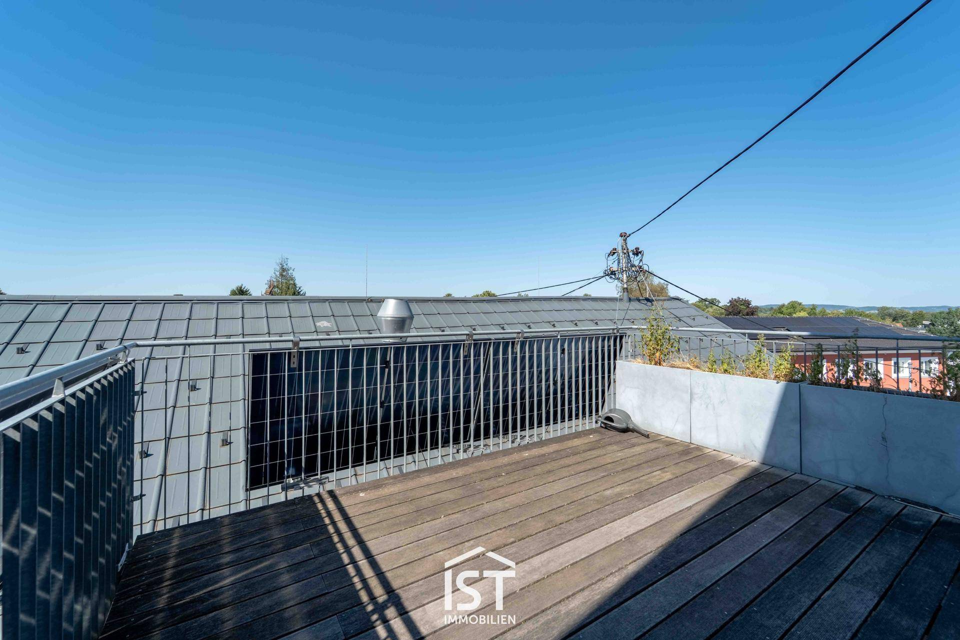 Geräumige Dachterrasse mit Holzboden und Metallgeländer, ideal für Entspannung im Freien.