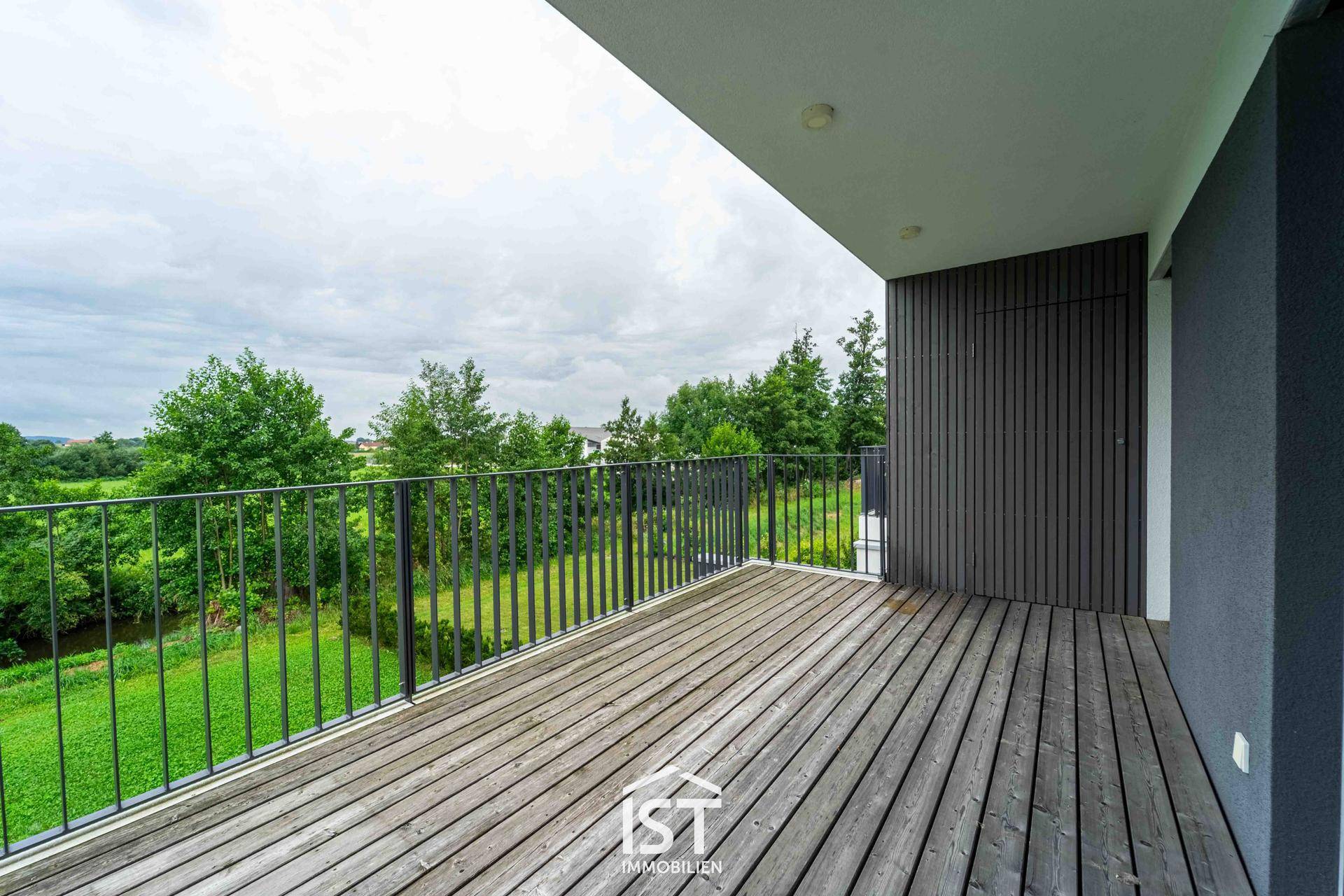Geräumiger Balkon mit Holzdielen und weitem Blick ins Grüne.