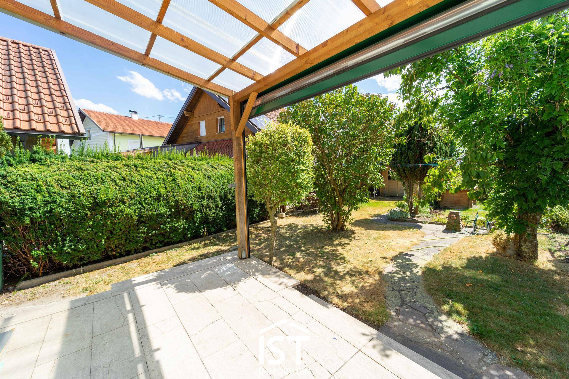 Überdachte Terrasse mit Steinplatten und Blick auf den gepflegten Gartenbereich.