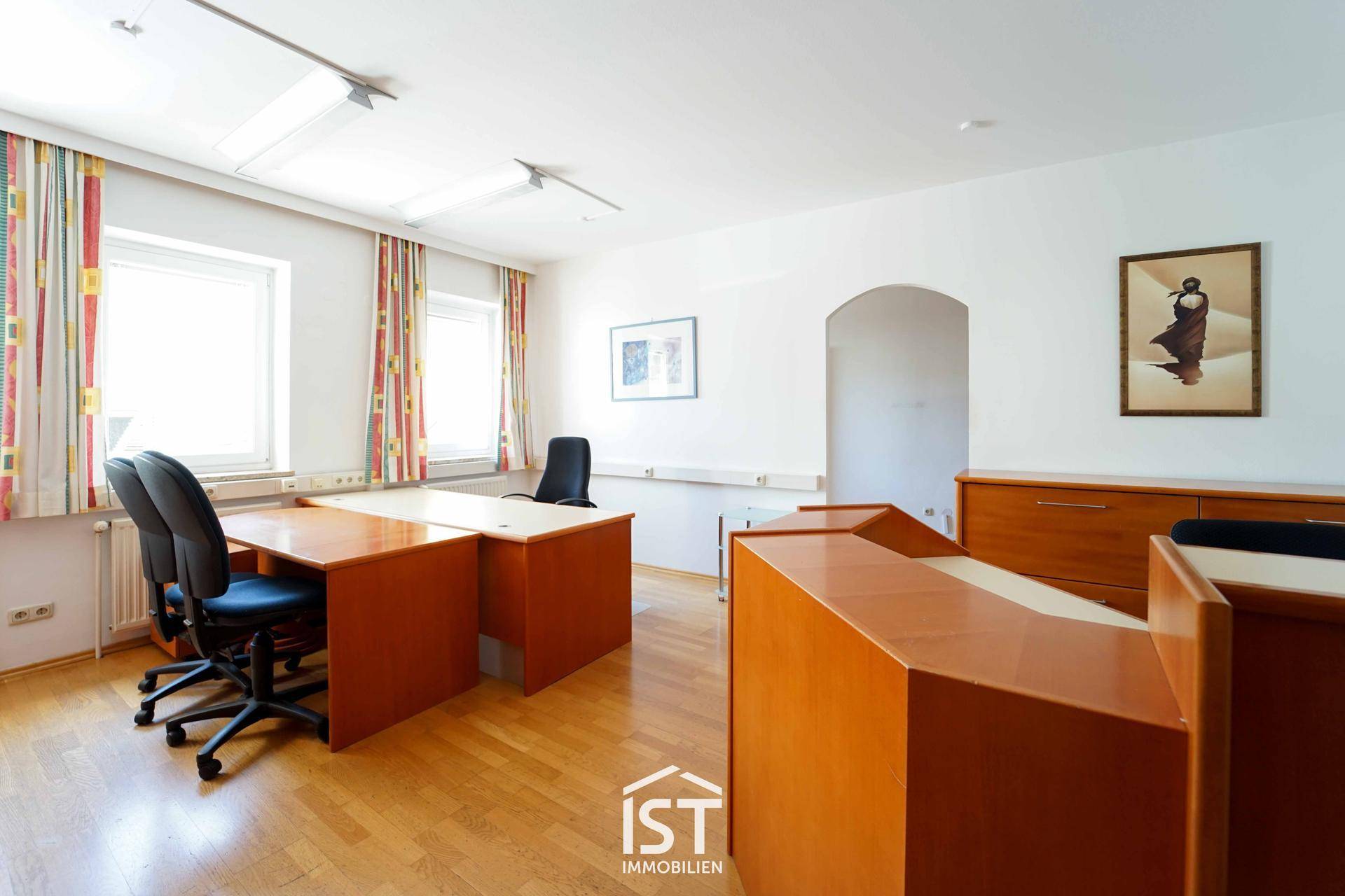 Funktionales Büro mit mehreren Arbeitsplätzen, Holzschreibtischen und Fenstern für Tageslicht.