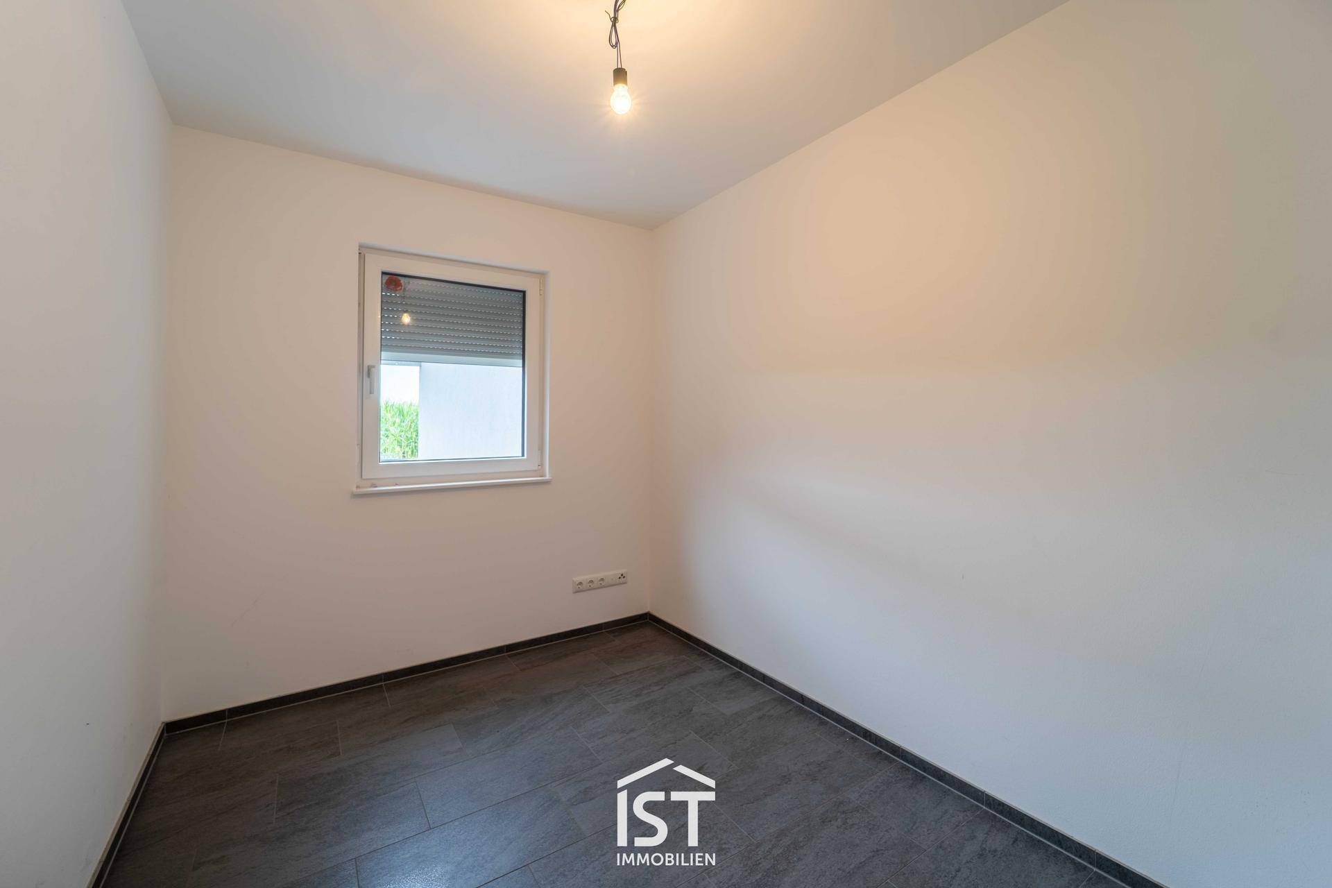 Helles Schlafzimmer mit grauem Fliesenboden und Fenster mit Rollladen.