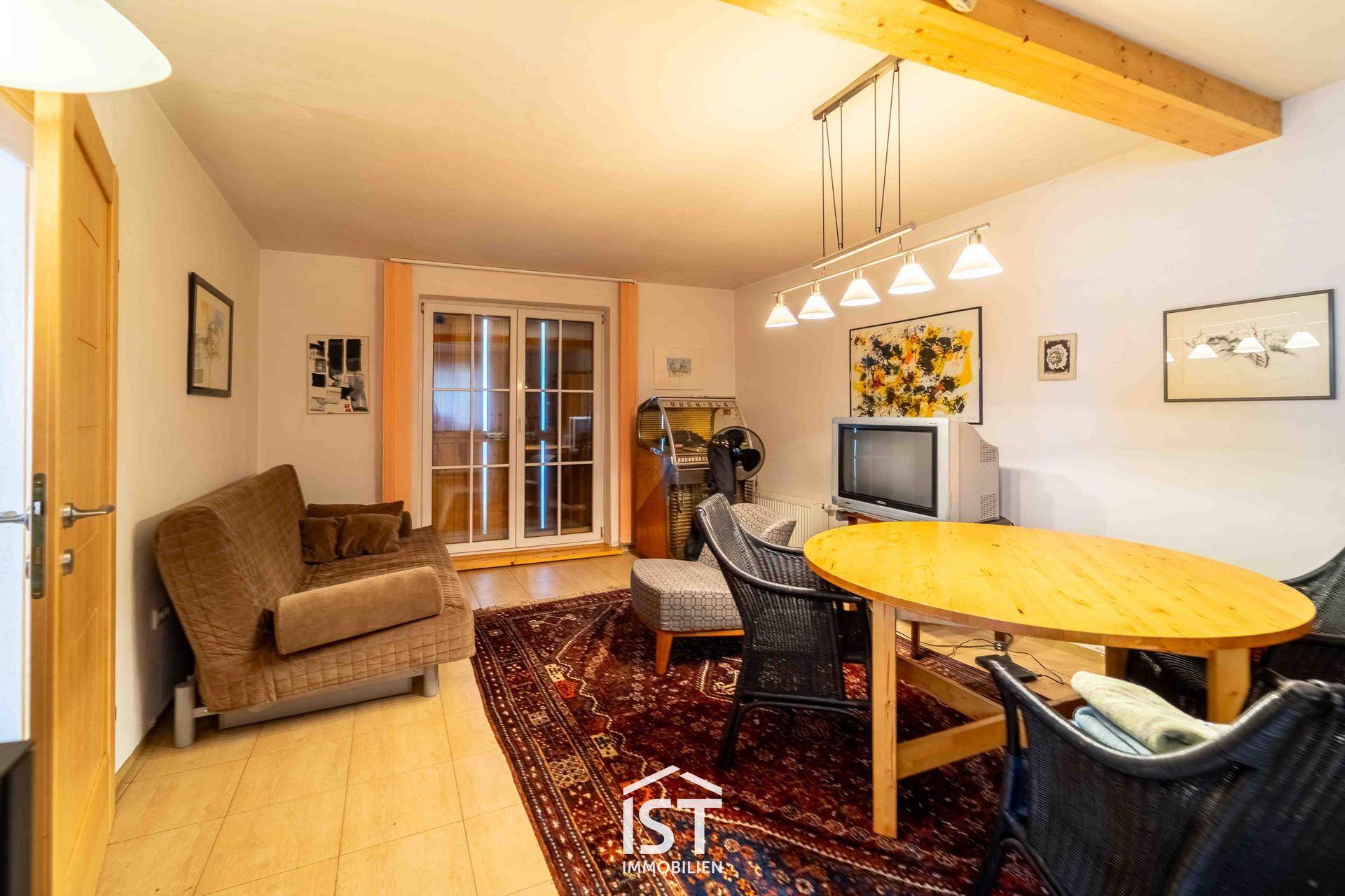 Gemütlicher Wohnbereich mit Esstisch, Sofa und sichtbaren Holzbalken an der Decke.