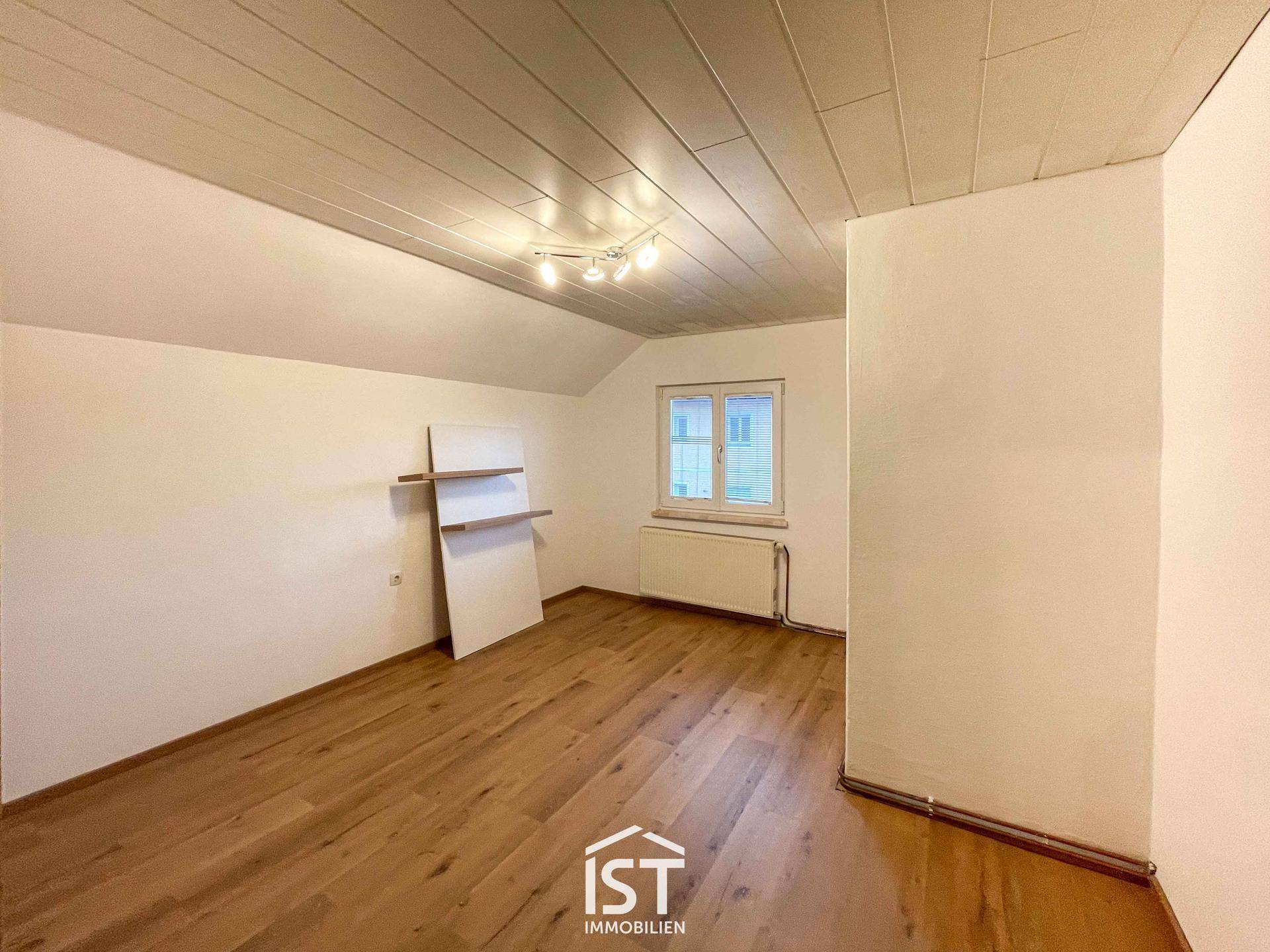 Helles Zimmer mit Holzboden, weißer Decke und einem Fenster, ideal als Schlaf- oder Arbeitszimmer.