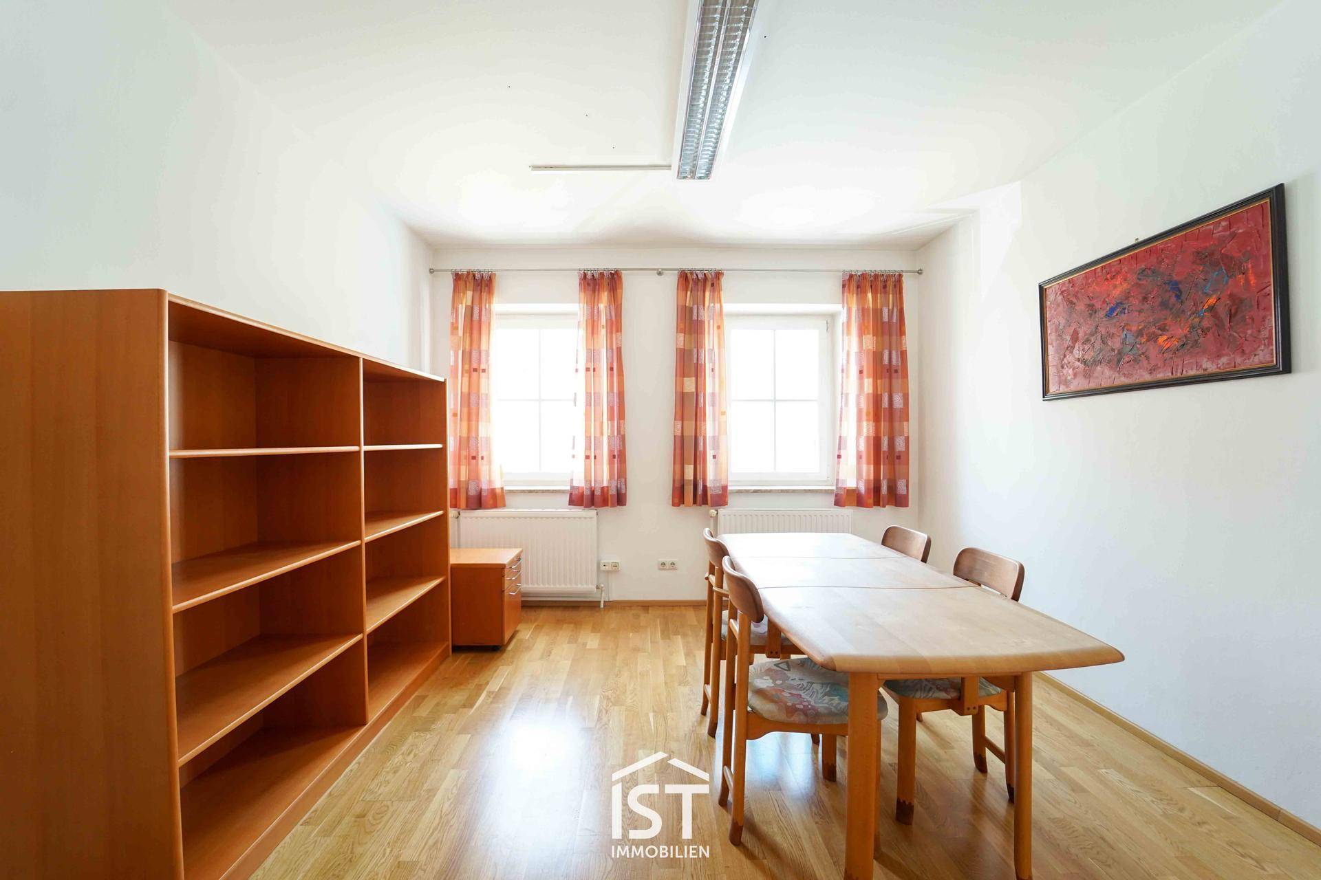 Besprechungsraum mit langem Holztisch, Stühlen und einem großen Bücherregal aus Holz.