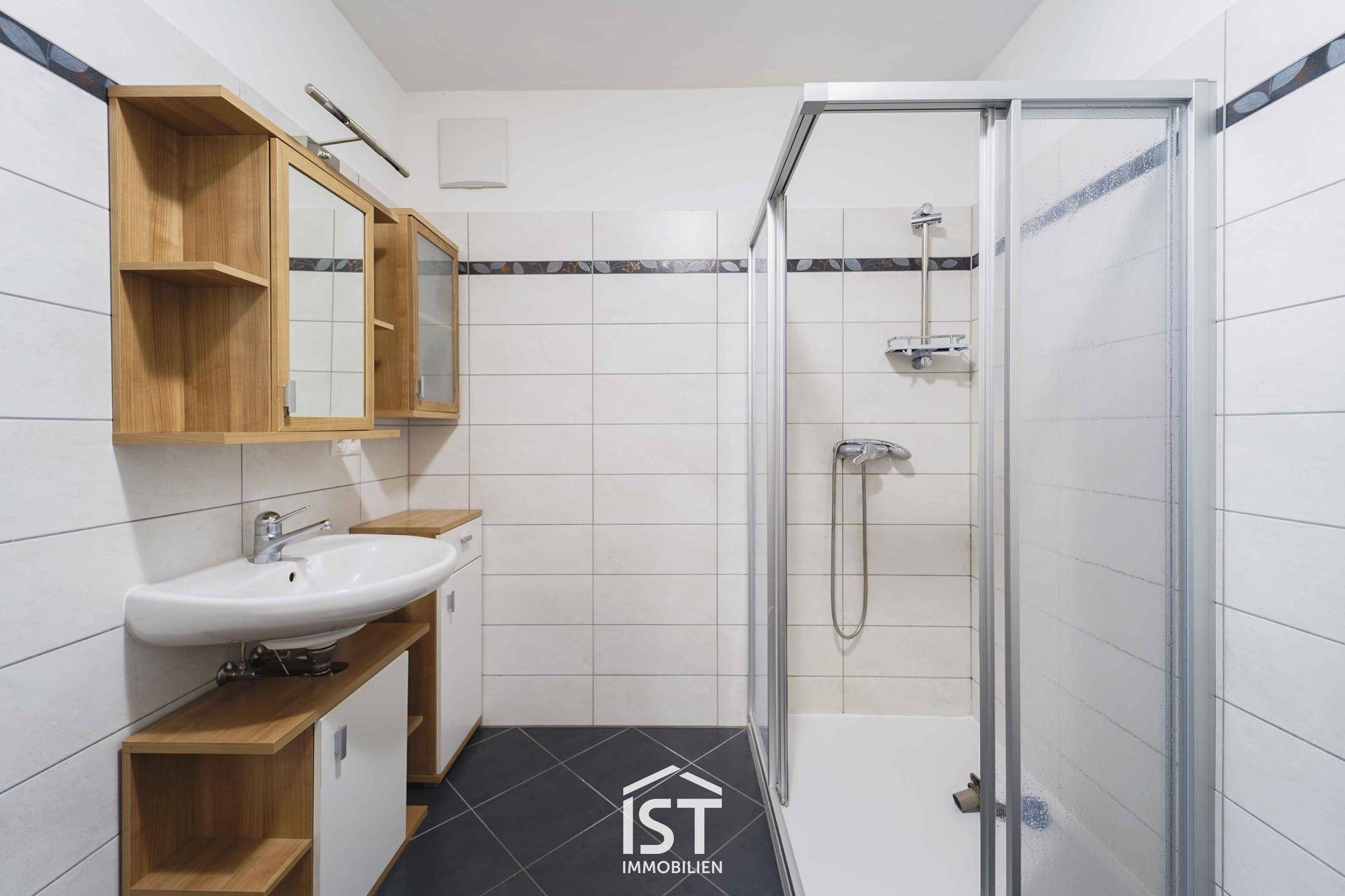 Badezimmer mit Duschkabine, Waschbecken und Holzschränken in neutralen Farben.