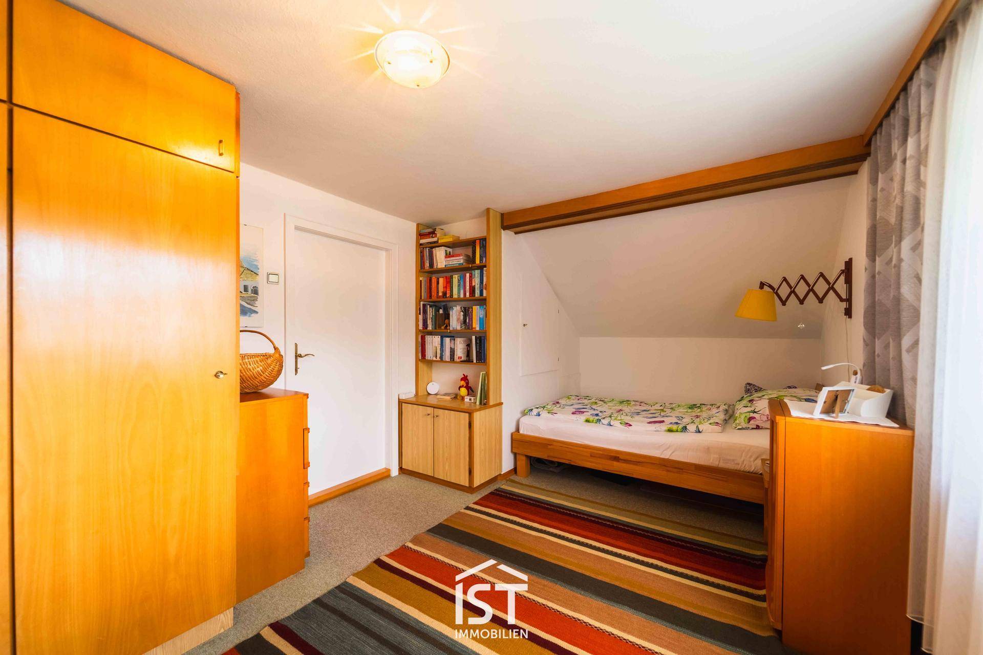 Gemütliches Schlafzimmer mit Holzbett, Teppichboden und Dachschräge, ideal als Gästezimmer.