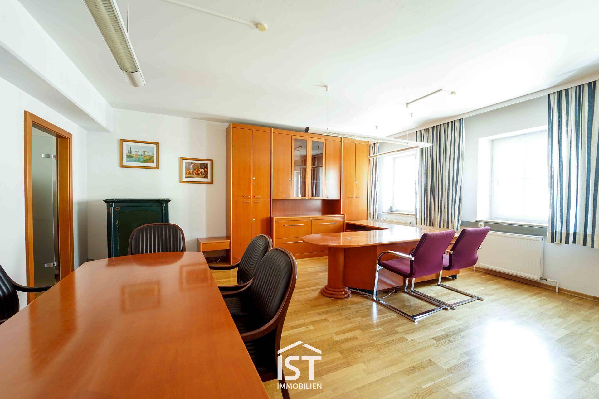 Geräumiges Büro mit Holzmöbeln, großem Schreibtisch und natürlichem Lichteinfall durch Fenster.