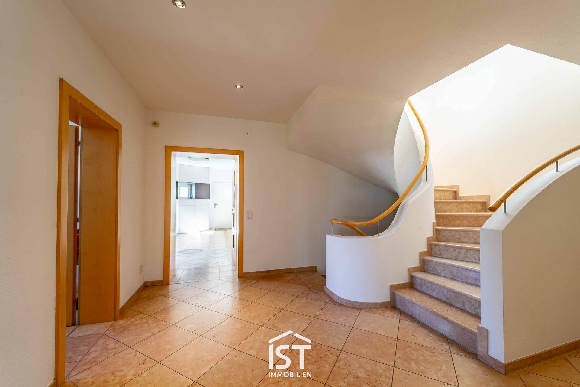 Geräumiger Flur mit geschwungener Treppe und Fliesenboden, der zu weiteren Räumen führt.