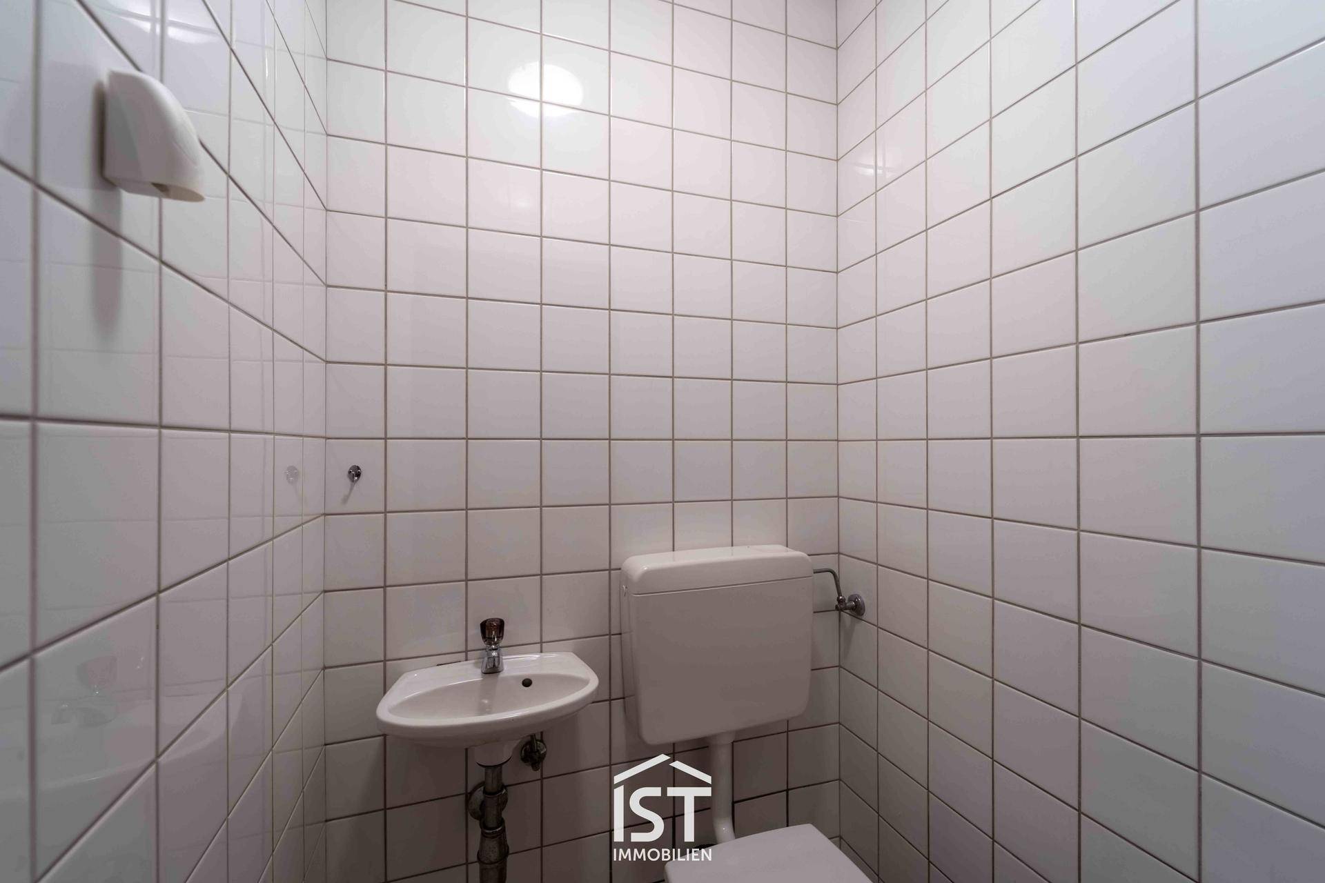 Kleines, vollständig gefliestes WC mit Toilette und Handwaschbecken.