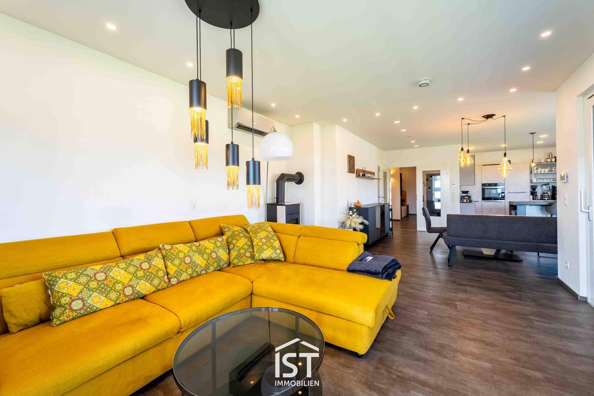 Lichtdurchflutetes Wohnzimmer mit gelbem Ecksofa und gemütlichem Kaminofen.