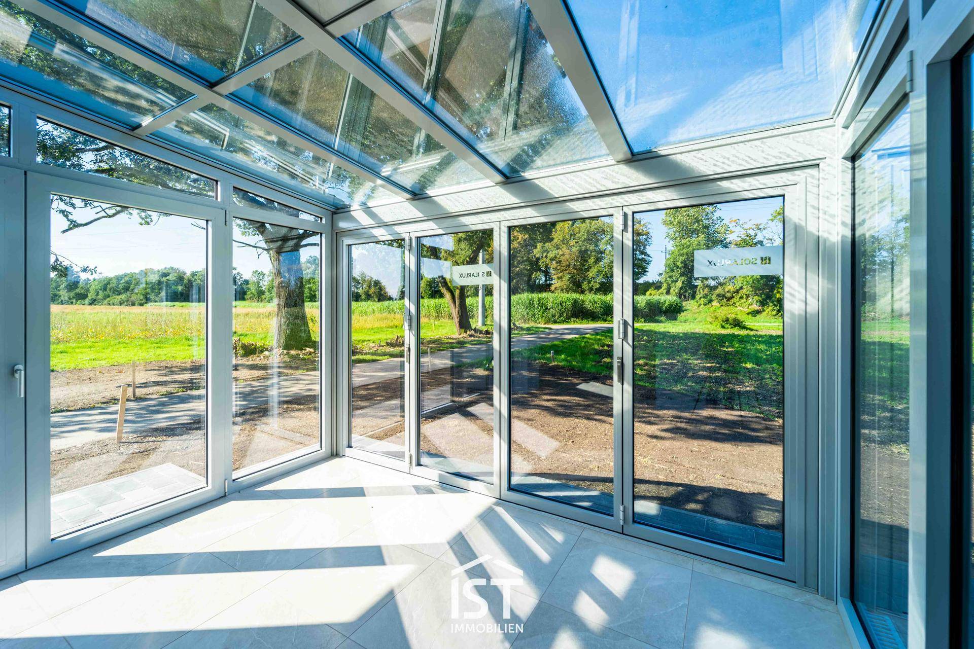Heller Wintergarten mit Glasdach und großen Fenstern, die einen weiten Blick ins Grüne bieten.