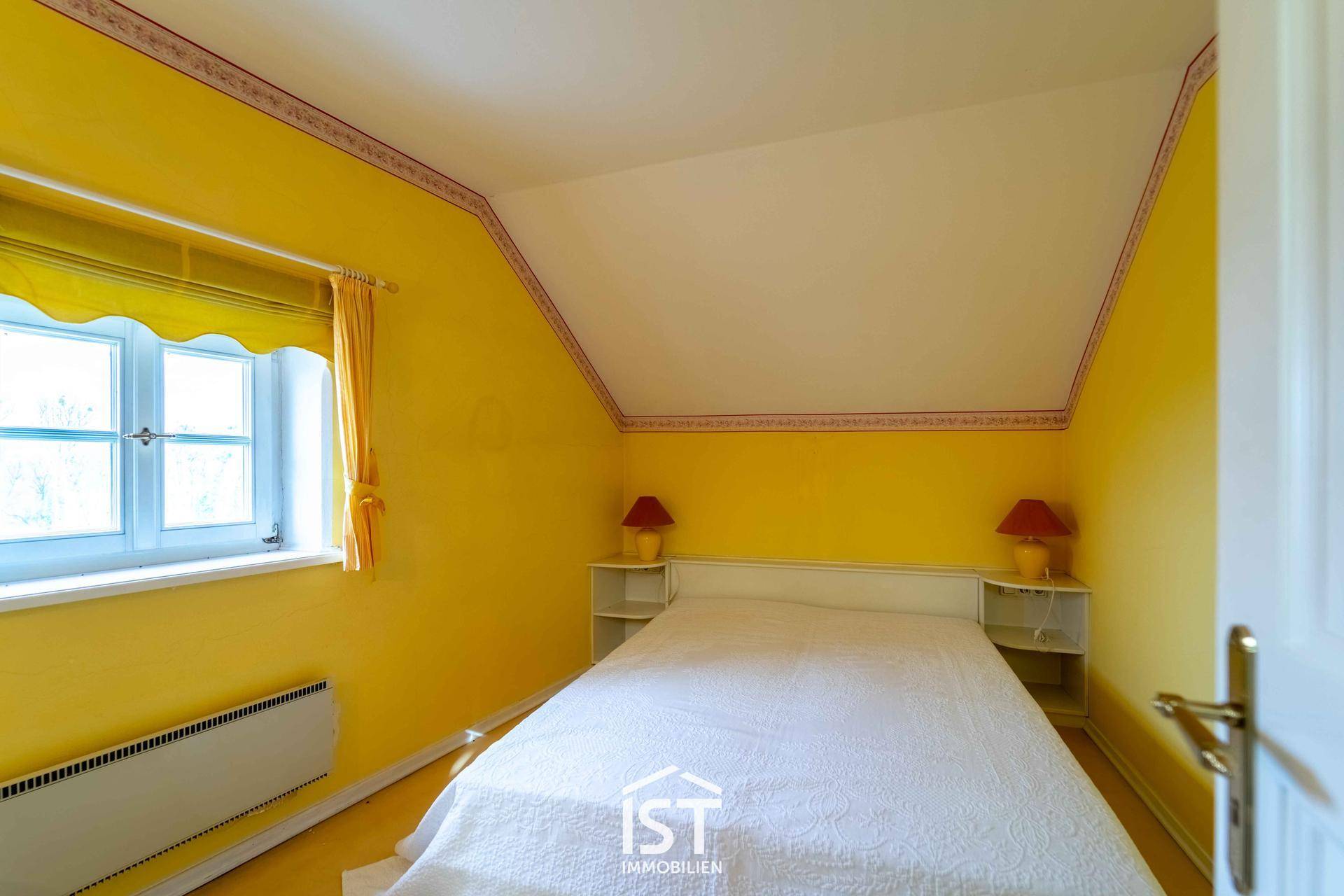Helles Schlafzimmer im Dachgeschoss mit gelben Wänden, Doppelbett und Dachschräge.