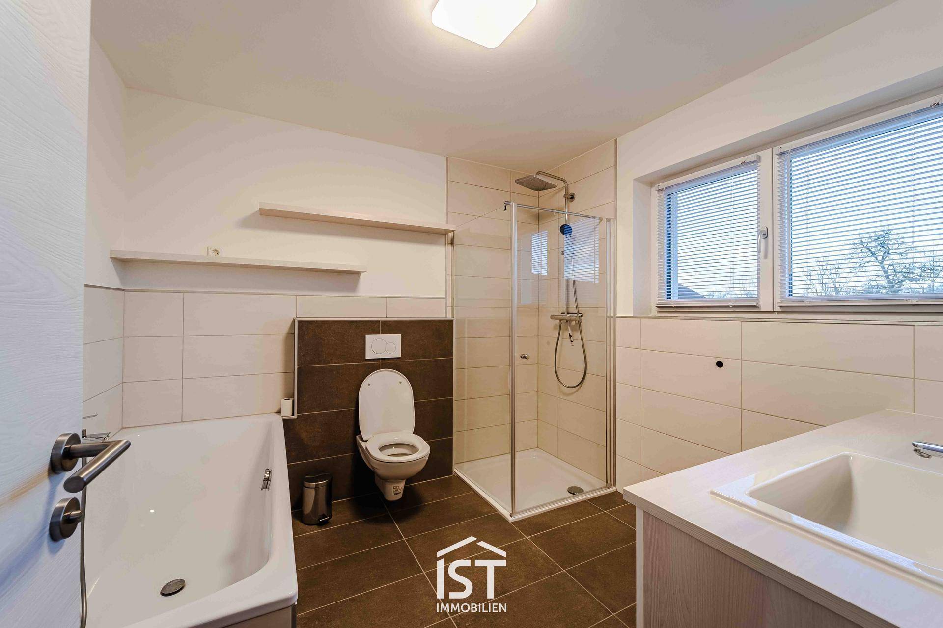 Helles Badezimmer mit Badewanne, Dusche, WC und Fenster.
