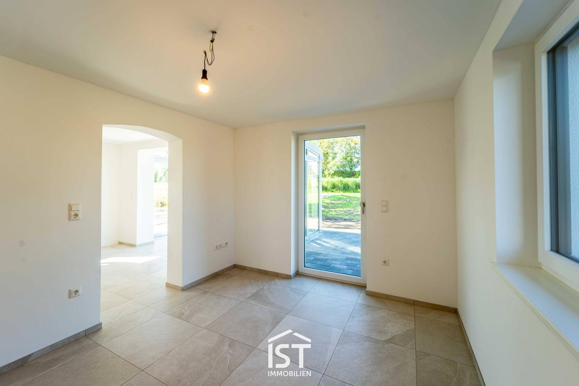 Leerer, heller Raum mit Fliesenboden und Zugang zum Garten, ideal als Wohnbereich.