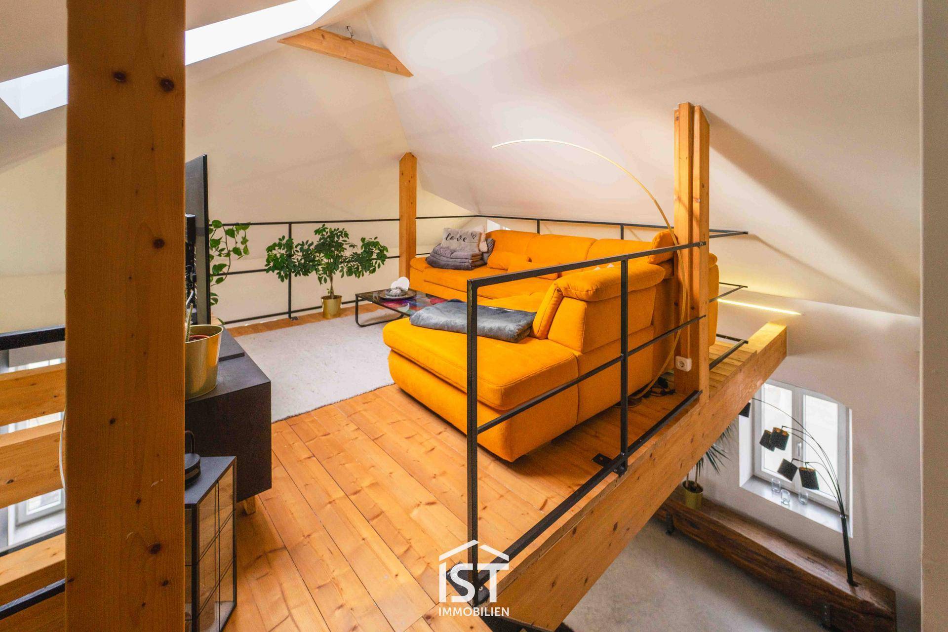 Gemütlicher Wohnbereich auf der Galerie mit gelbem Sofa, Holzboden und Dachfenster.