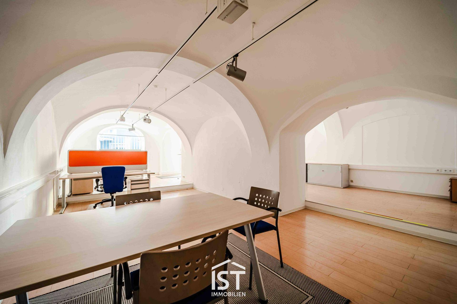 Weitläufiger Bürobereich mit mehreren Arbeitsplätzen, Gewölbedecken und Blick auf den vorderen Eingangsbereich mit Schaufenstern.