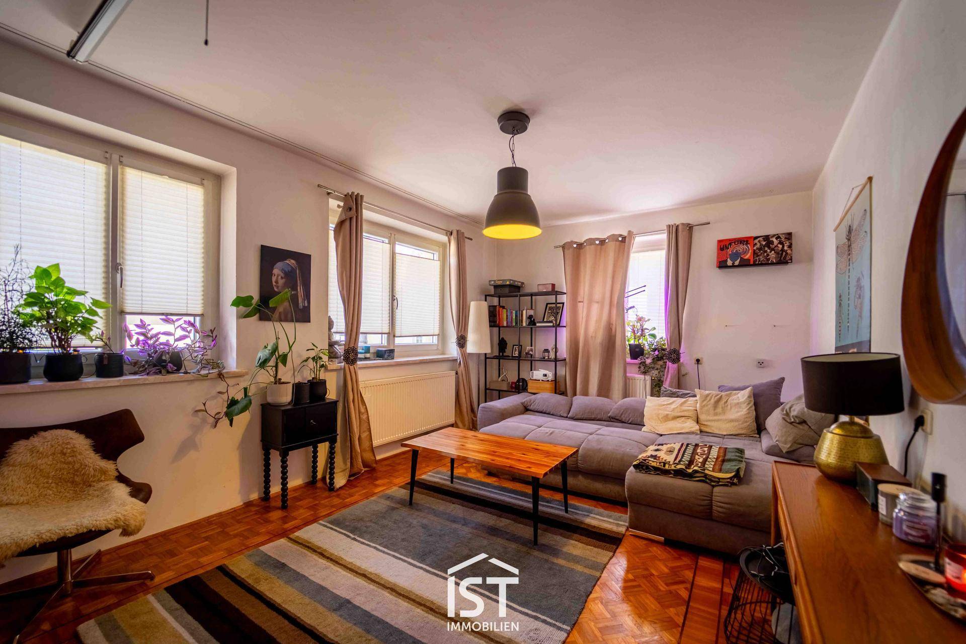 Helles Wohnzimmer mit bequemer Couch, Holztisch und mehreren Fenstern für eine freundliche Atmosphäre.