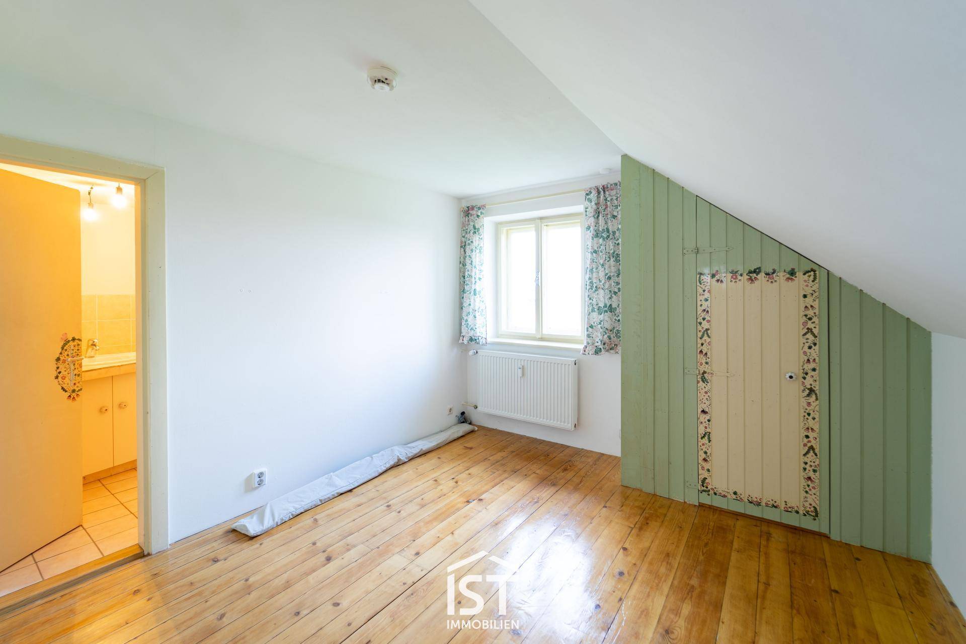 Schlafzimmer mit Holzboden, Dachschräge und grüner Wandverkleidung.