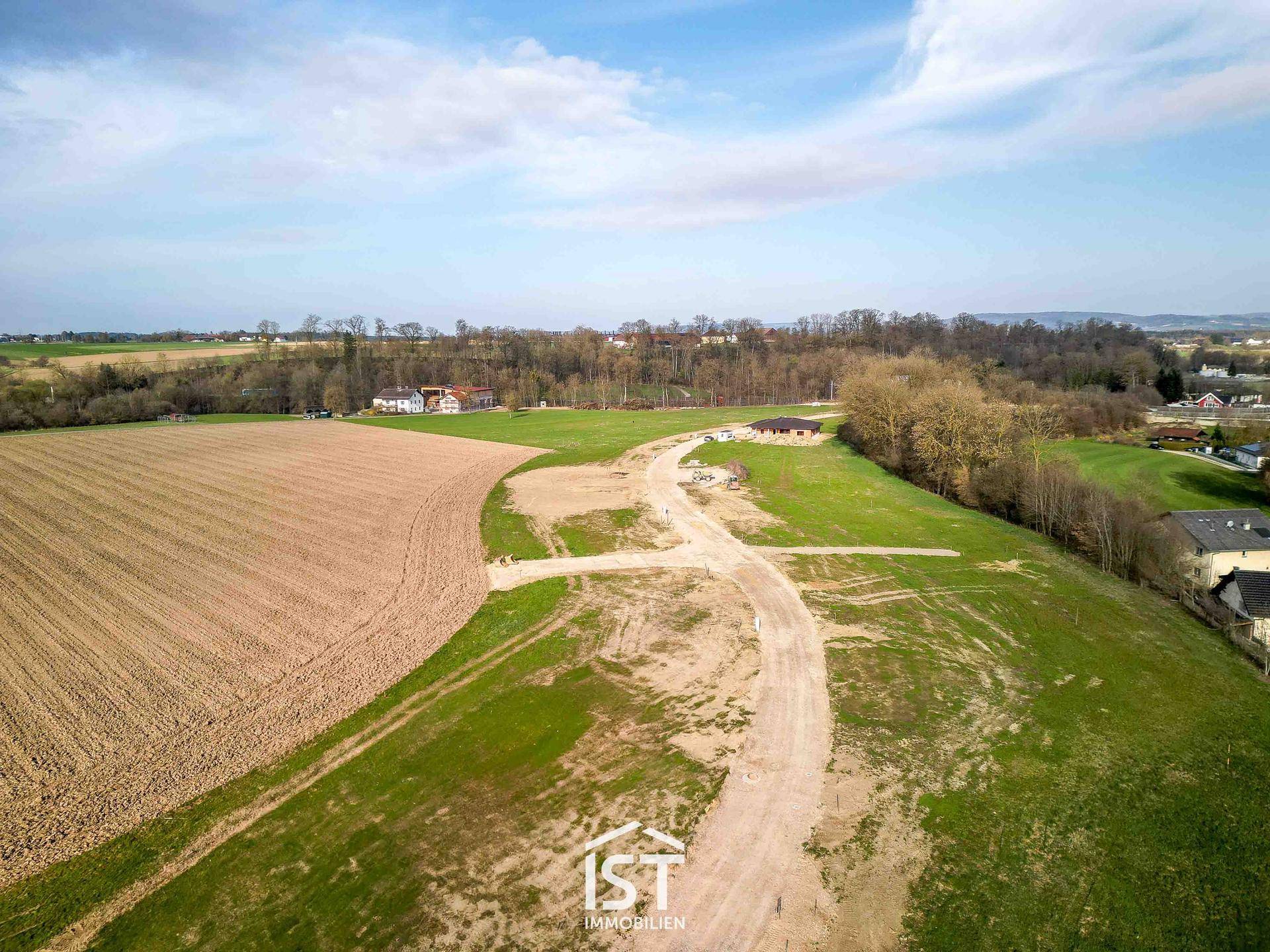 Weitläufige Luftaufnahme einer ländlichen Landschaft mit Feldern, Wäldern und einer neuen Zufahrtsstraße.