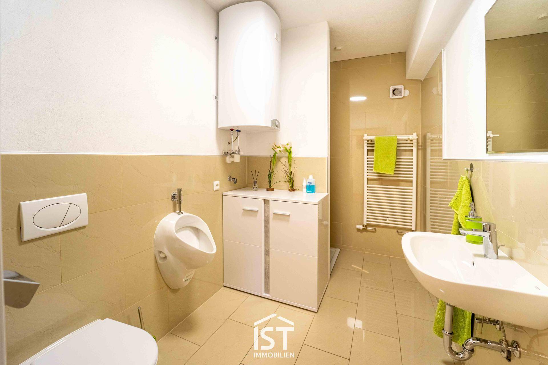 Modernes Badezimmer mit beigefarbenen Fliesen, Urinal, Toilette, Waschbecken und einem Handtuchheizkörper.