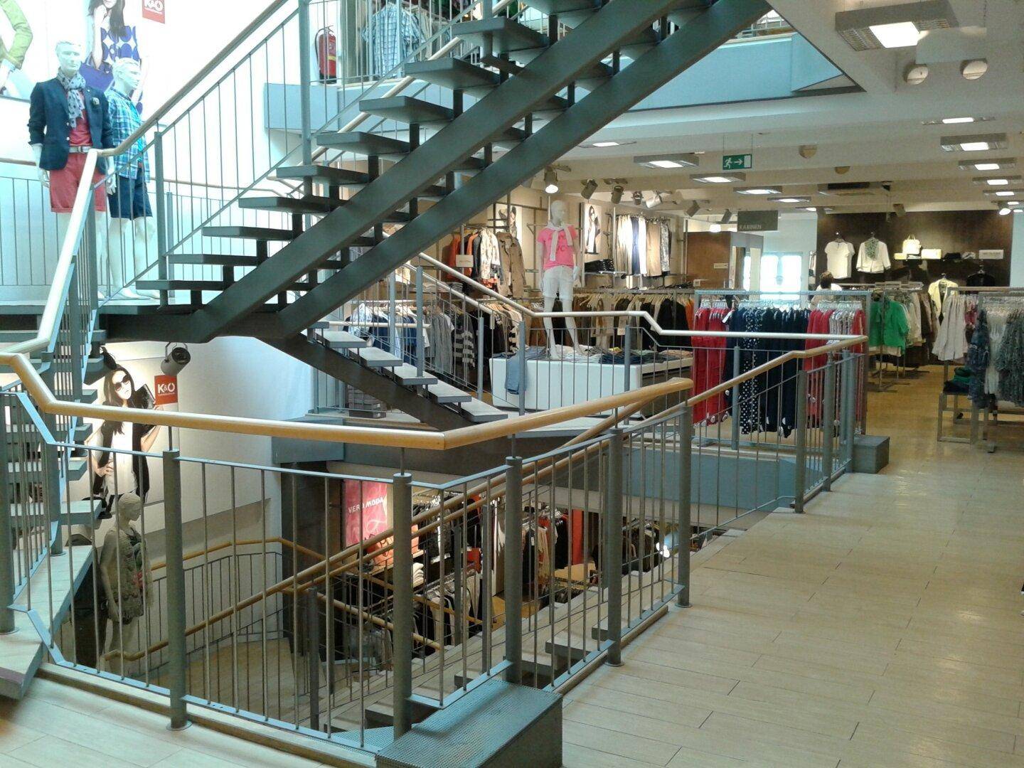 Geräumiger Verkaufsraum auf mehreren Ebenen mit moderner Metalltreppe und zahlreichen Kleiderständern.