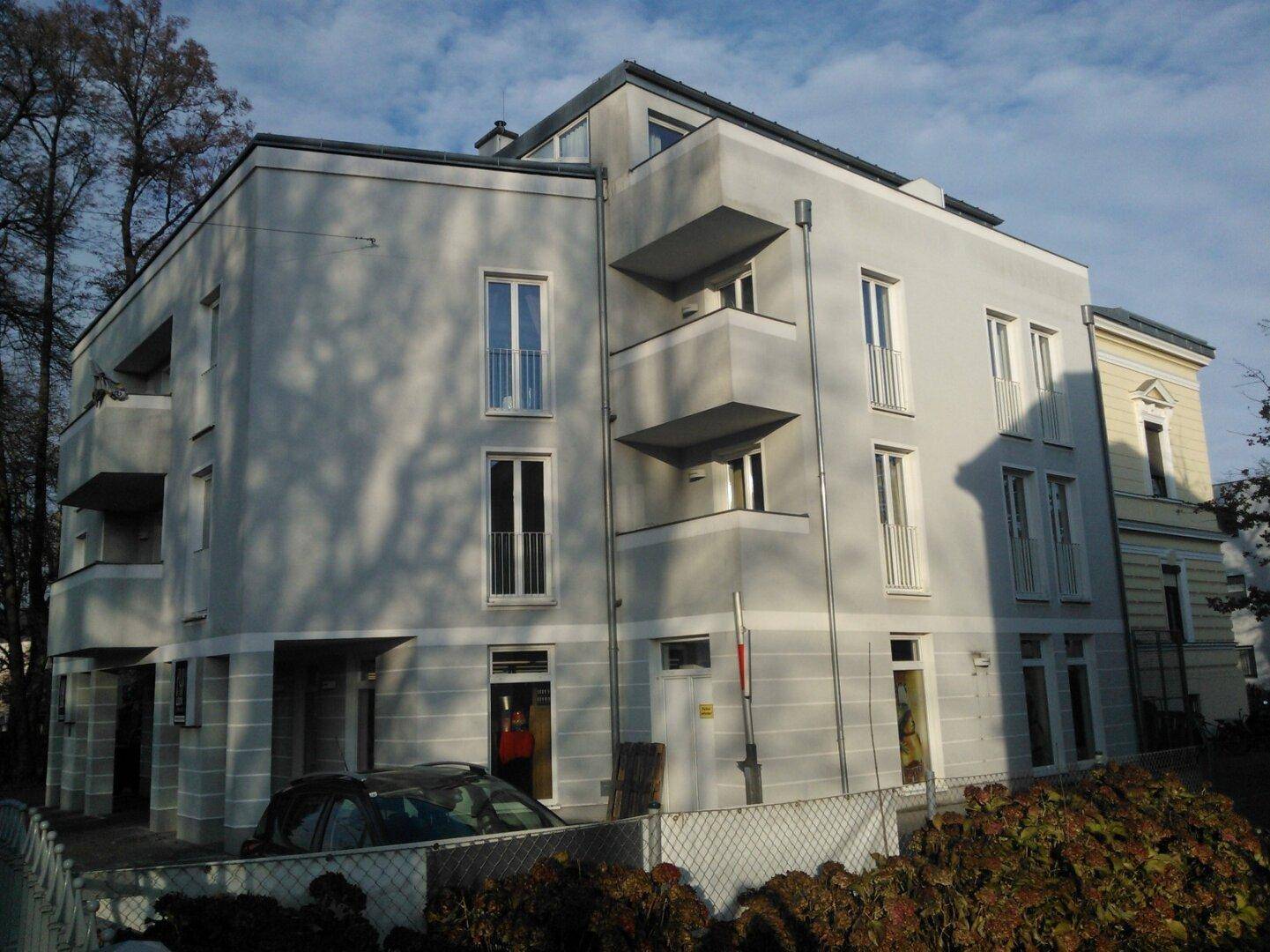 Modernes Mehrfamilienhaus mit heller Fassade, großen Fenstern und Balkonen in grüner Umgebung.