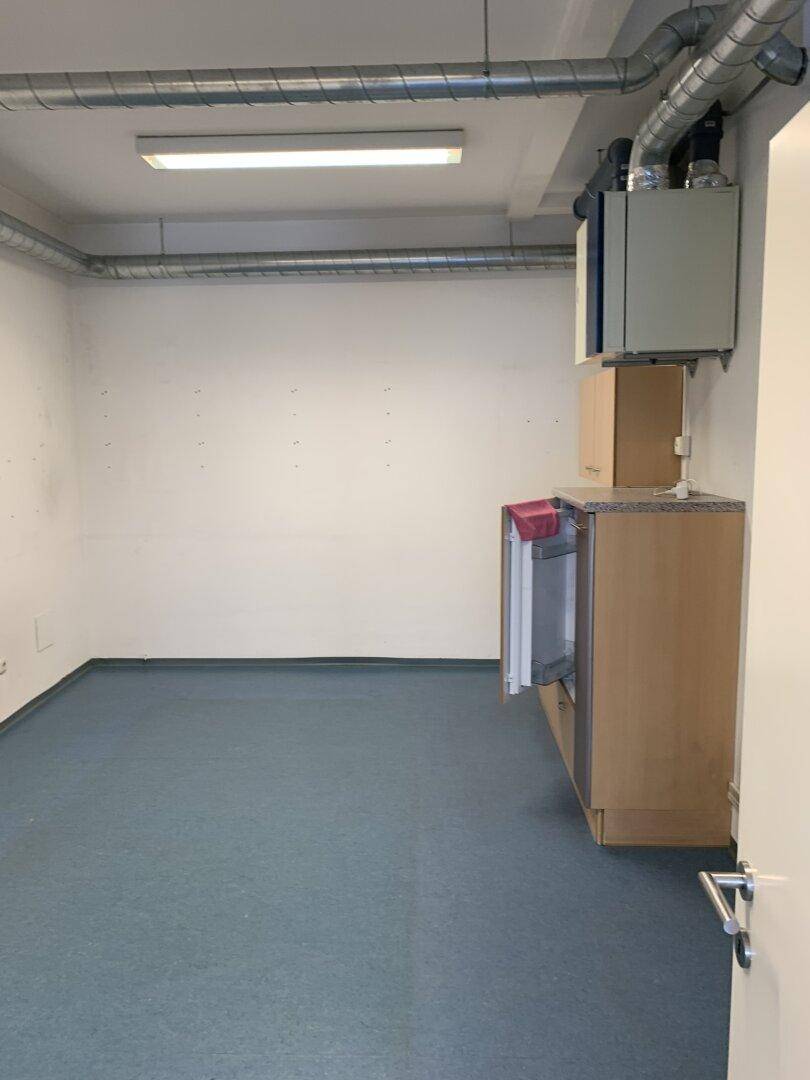 Gewerberaum mit integrierter Küchenzeile, blauer Boden und sichtbaren Lüftungsrohren an der Decke.