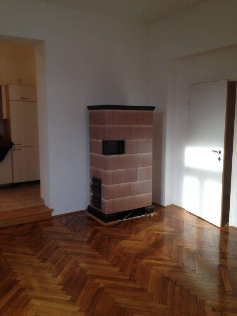 Detailansicht eines traditionellen Kachelofens in einem hellen Raum mit Fischgrätparkett.