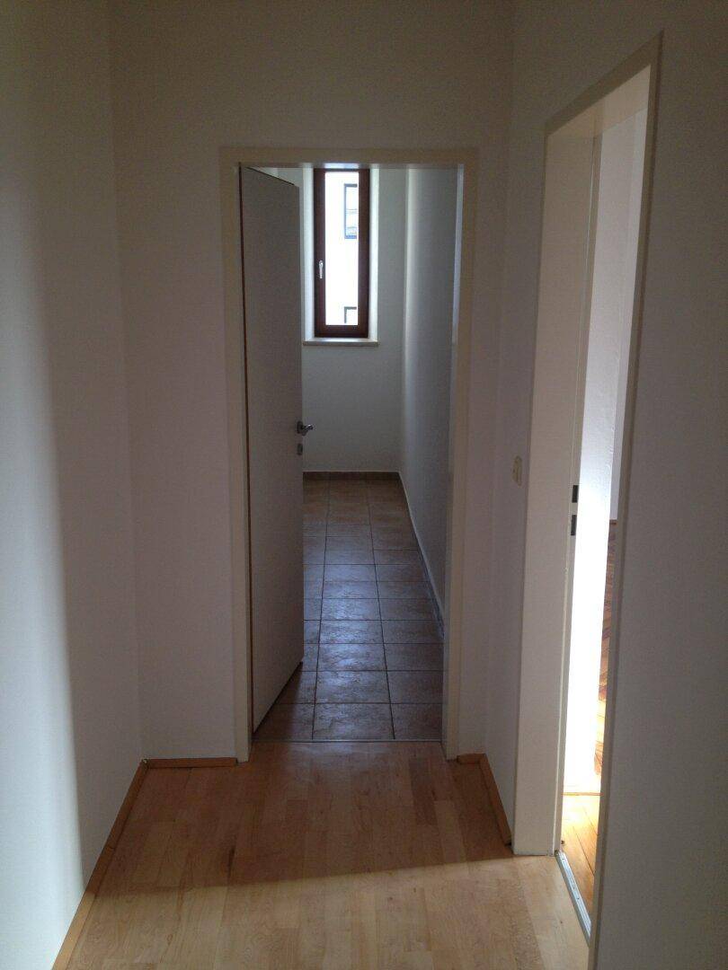 Heller Flur mit Holzboden, der zu einem weiteren Bereich mit Fliesenboden führt.