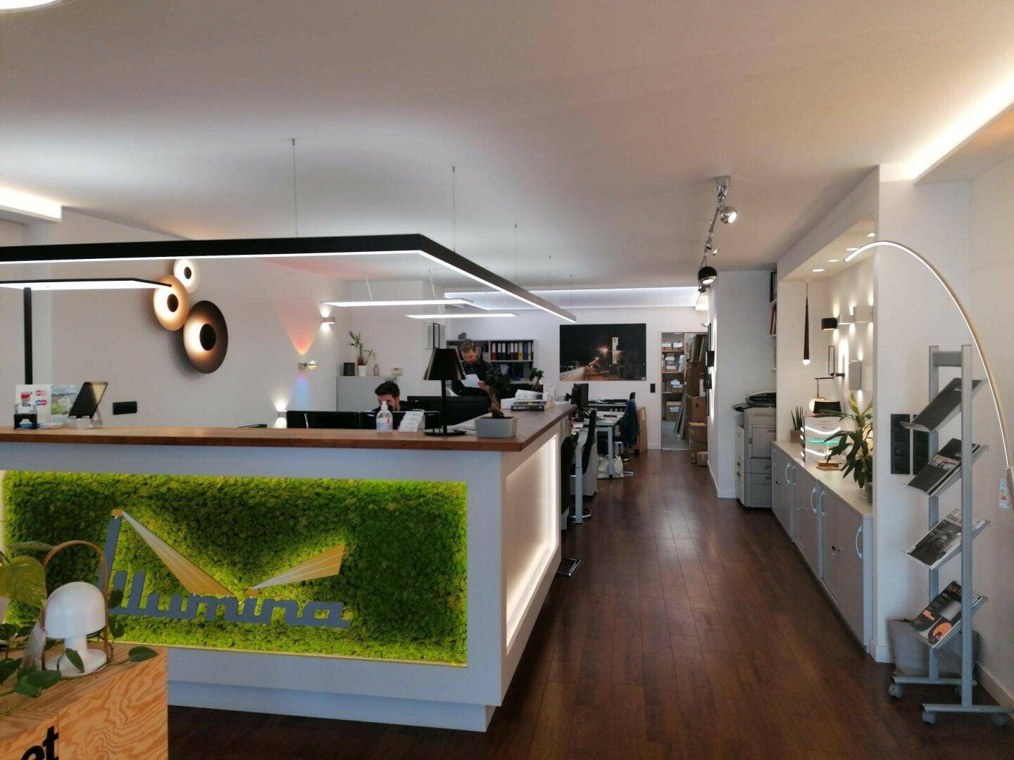 Empfangsbereich eines modernen Büros mit Holzboden, Mooswand-Dekoration und indirekter Beleuchtung.