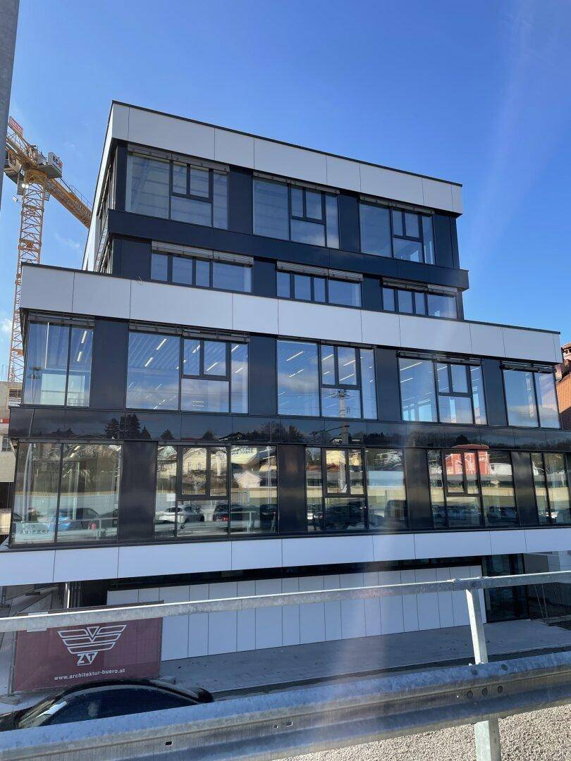 Ansicht eines modernen Bürogebäudes mit großen Fenstern und einer Baustelle im Hintergrund.