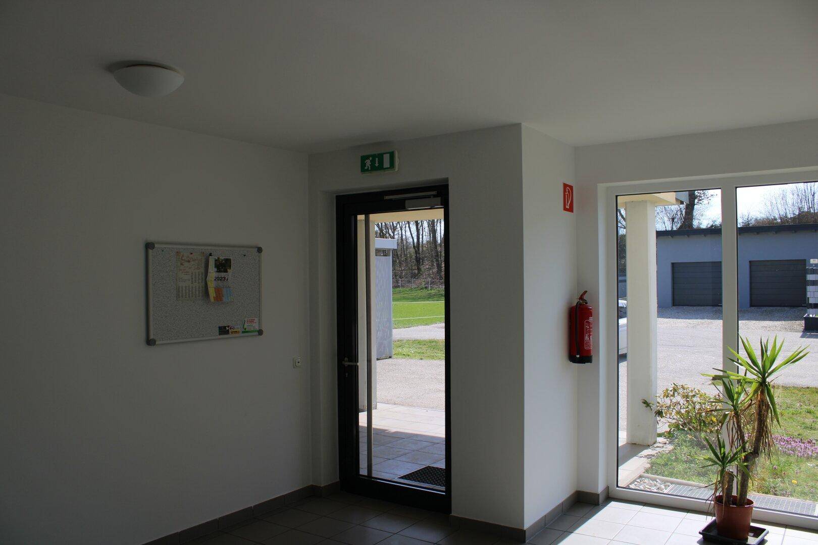Heller Eingangsbereich mit Fliesenboden, Glastür und Blick ins Grüne.