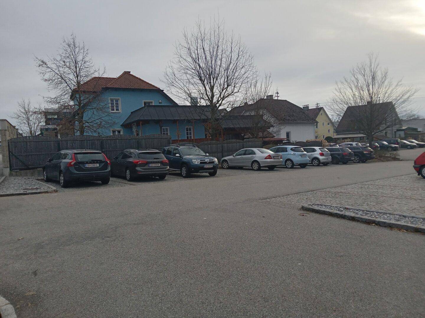 Ein Parkplatz mit mehreren Autos vor einer Reihe von Gebäuden unter einem bewölkten Himmel.