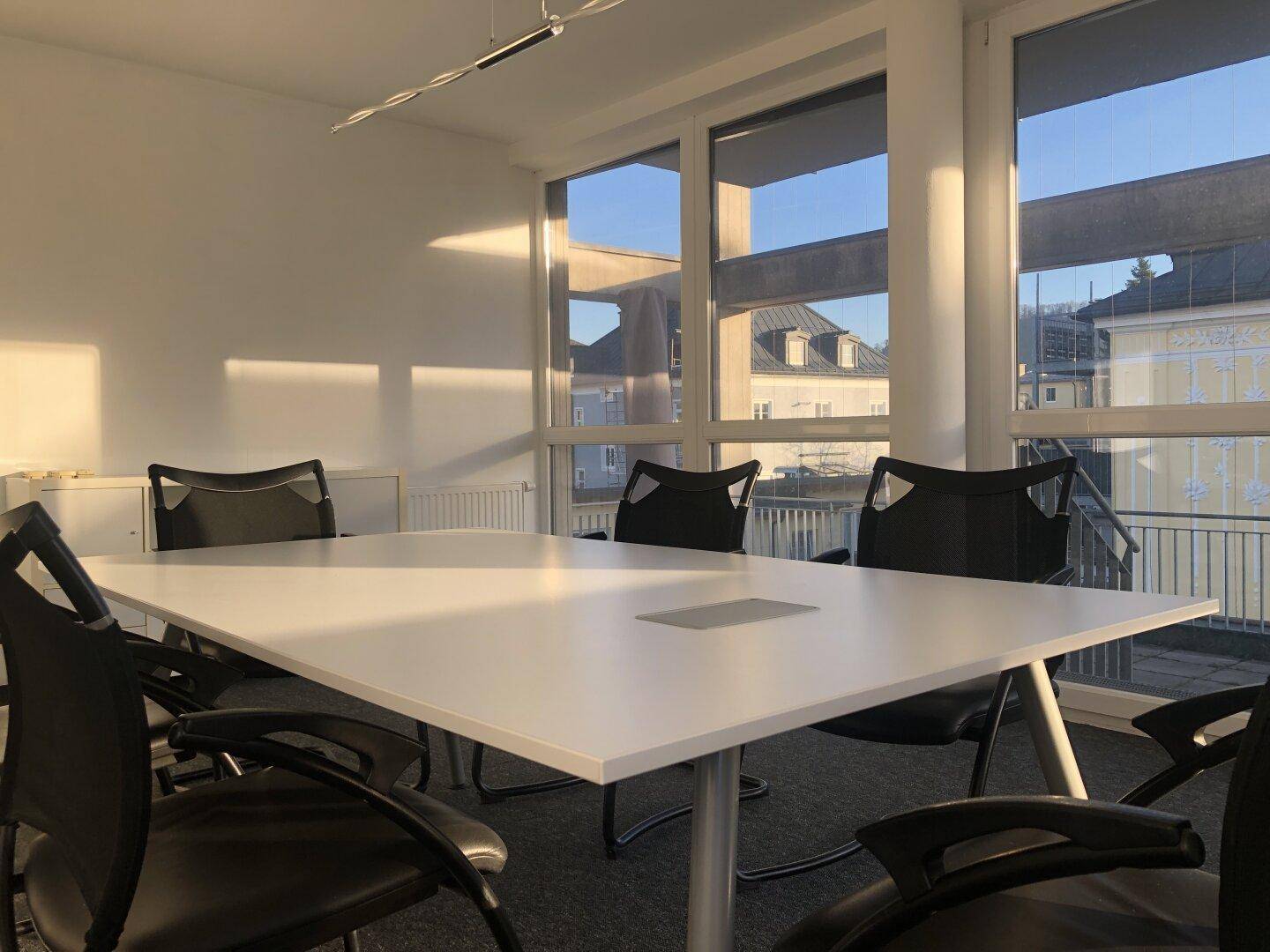Heller Konferenzraum mit großem Besprechungstisch und Stühlen, umgeben von großen Fenstern mit Blick nach draußen.