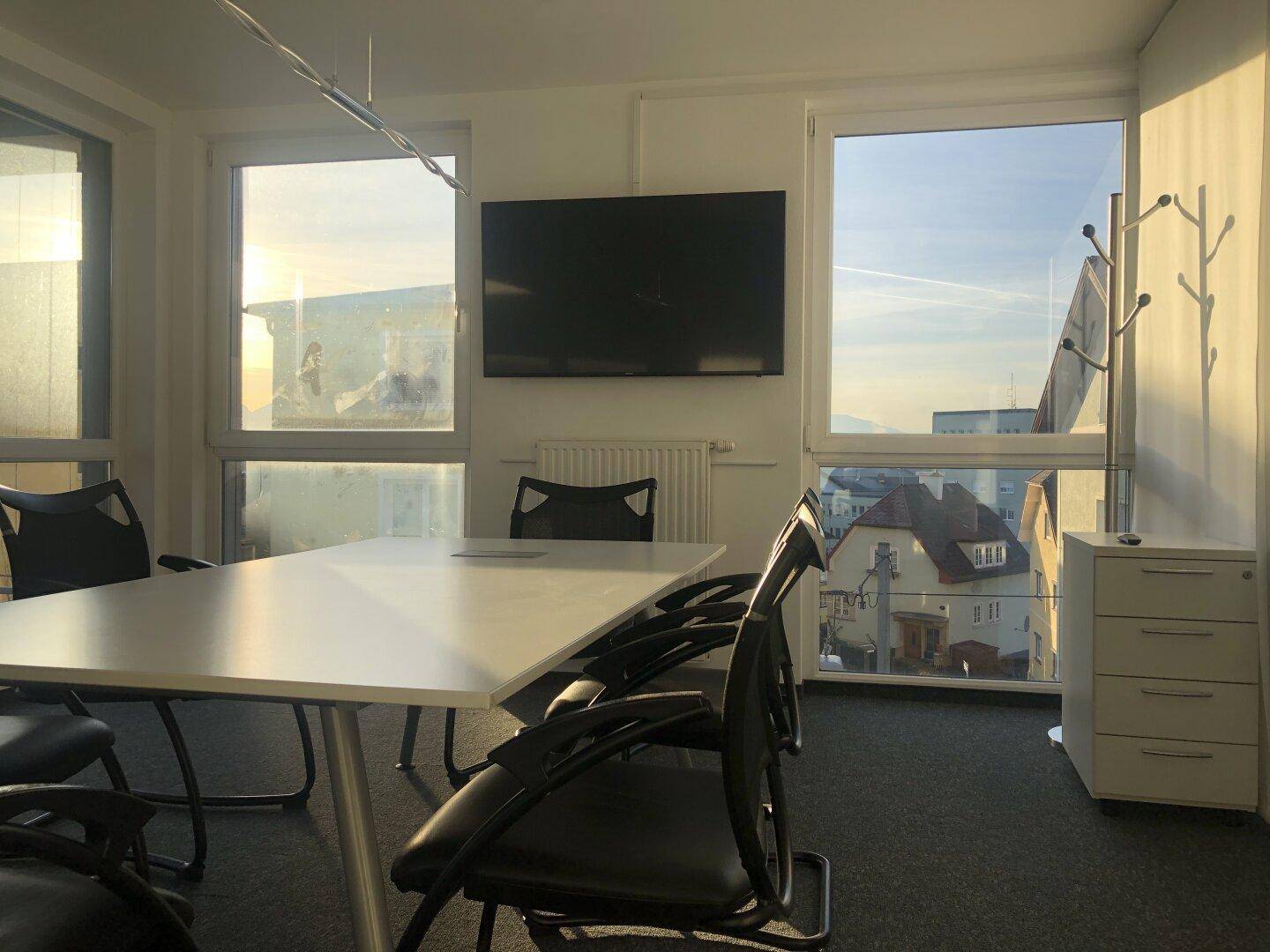 Konferenzraum mit großem Tisch, bequemen Stühlen und einem Wandfernseher, bietet eine weite Aussicht.