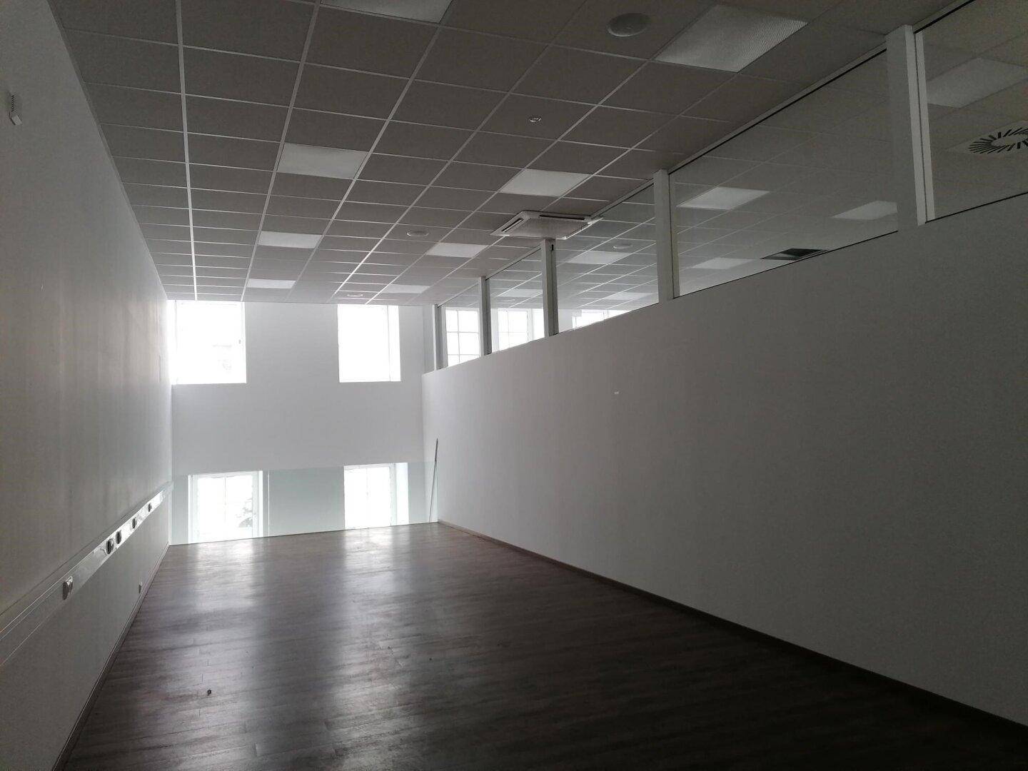 Langer, heller Büroraum mit hohen Decken und großen Fenstern, die viel Tageslicht hereinlassen.