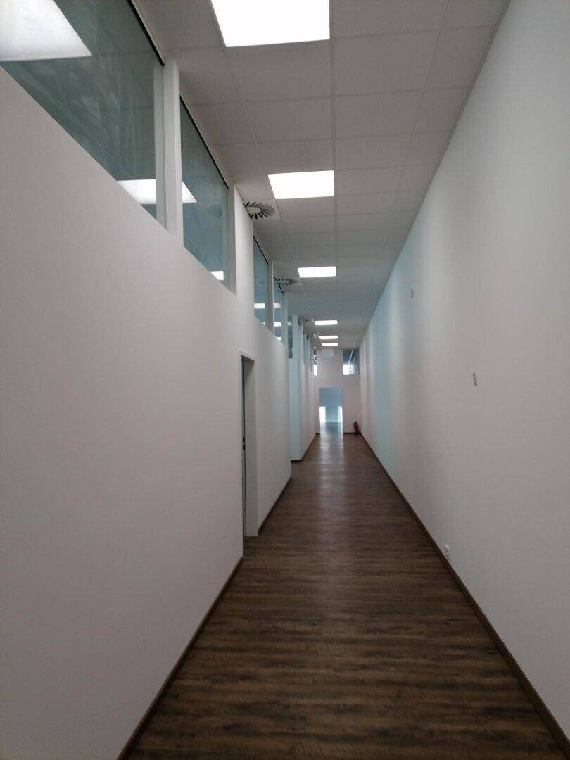 Langer, moderner Flur mit Laminatboden und weißen Wänden, der zu weiteren Räumen führt.