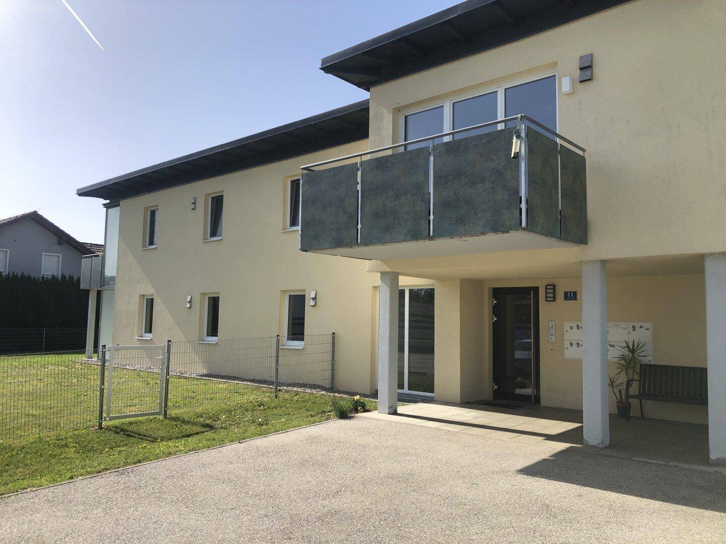 Modernes Mehrfamilienhaus mit Eingangsbereich, Balkon und Carport-Stellplätzen.