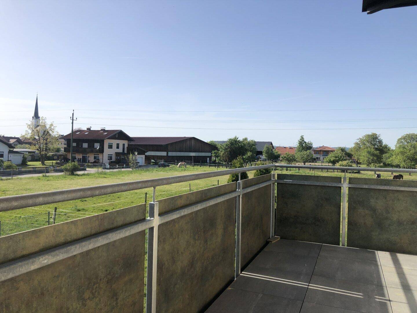 Balkon mit weitem Blick über grüne Felder, Pferde und eine Kirche in der Ferne.