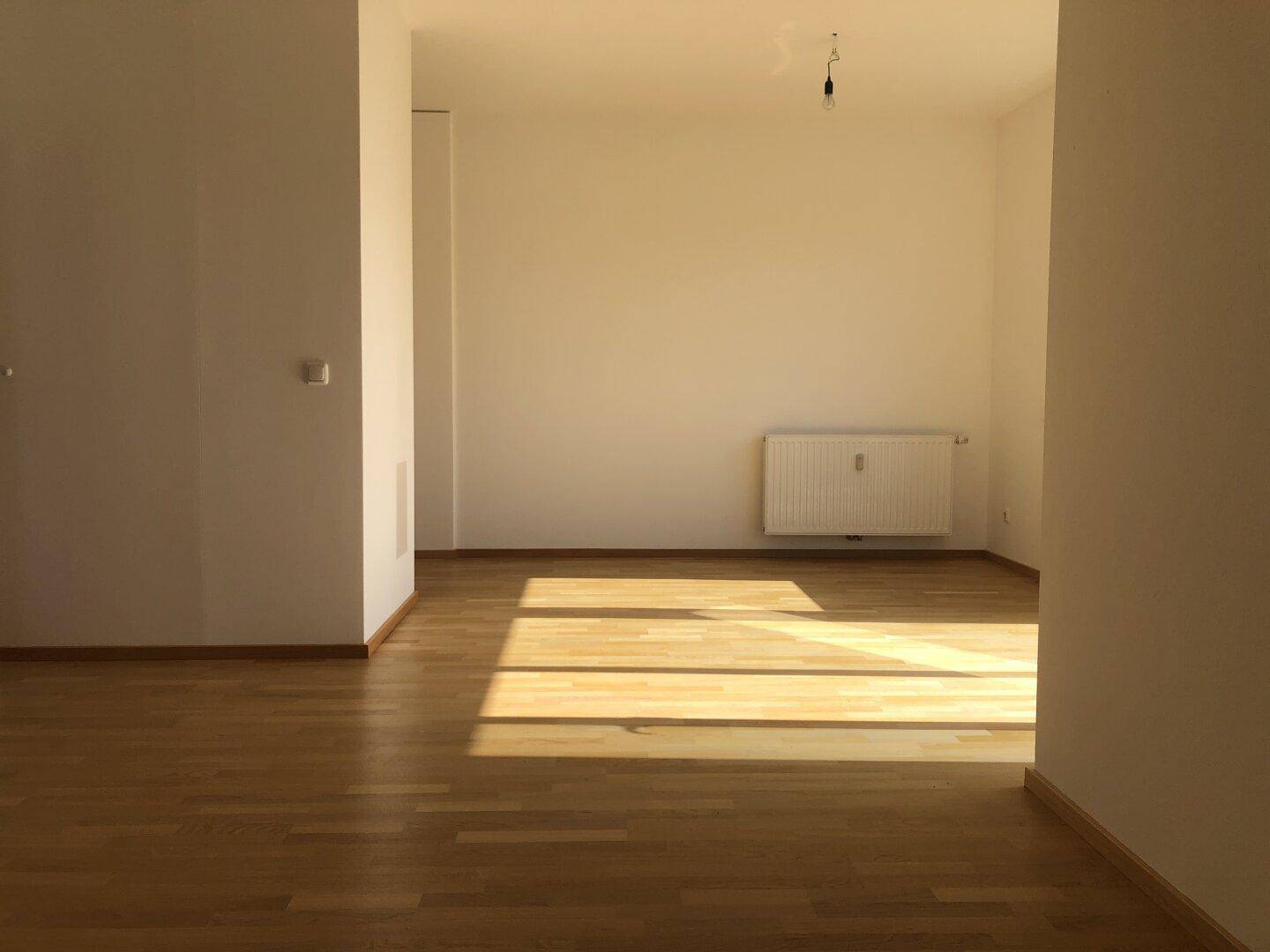 Geräumiger Wohnraum mit hellem Parkettboden und viel natürlichem Licht durch große Fenster.