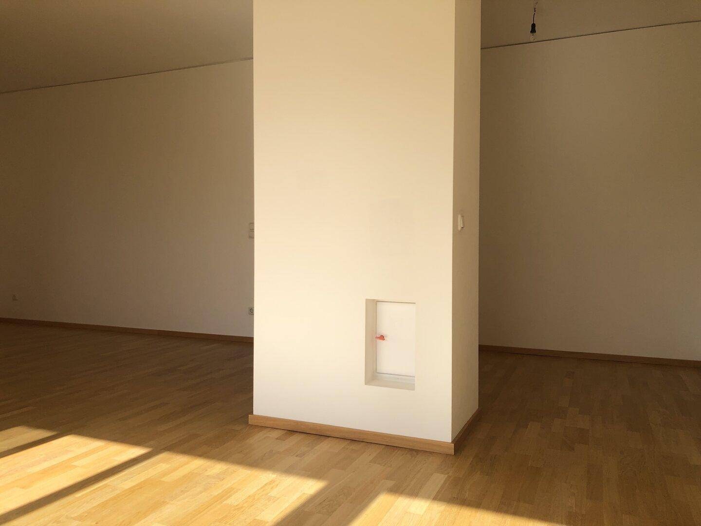 Heller Wohnraum mit Parkettboden und einem zentralen Pfeiler, durchflutet von Sonnenlicht.