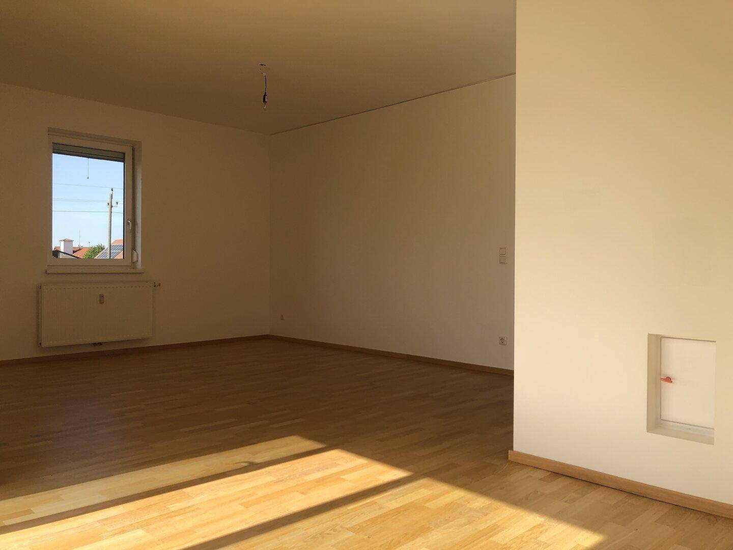 Heller Wohnraum mit Parkettboden und einem Fenster, das viel Tageslicht hereinlässt.