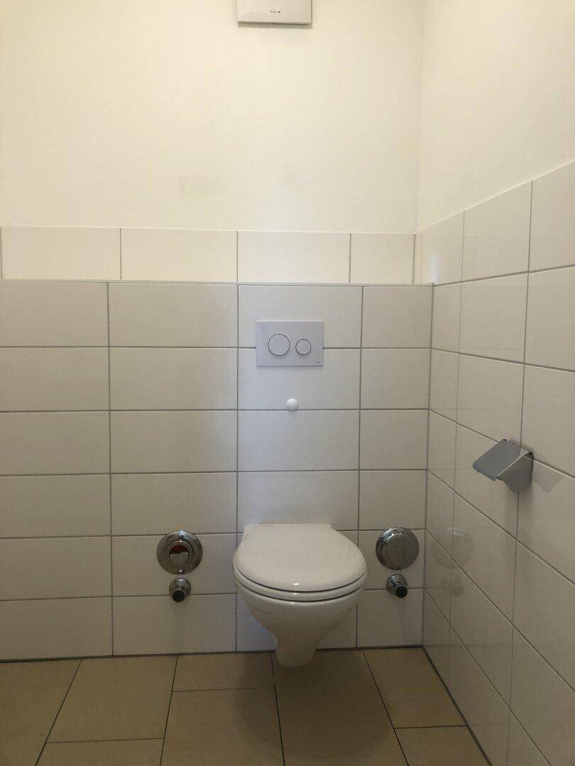 Separates WC mit weißen Fliesen und einer wandhängenden Toilette.