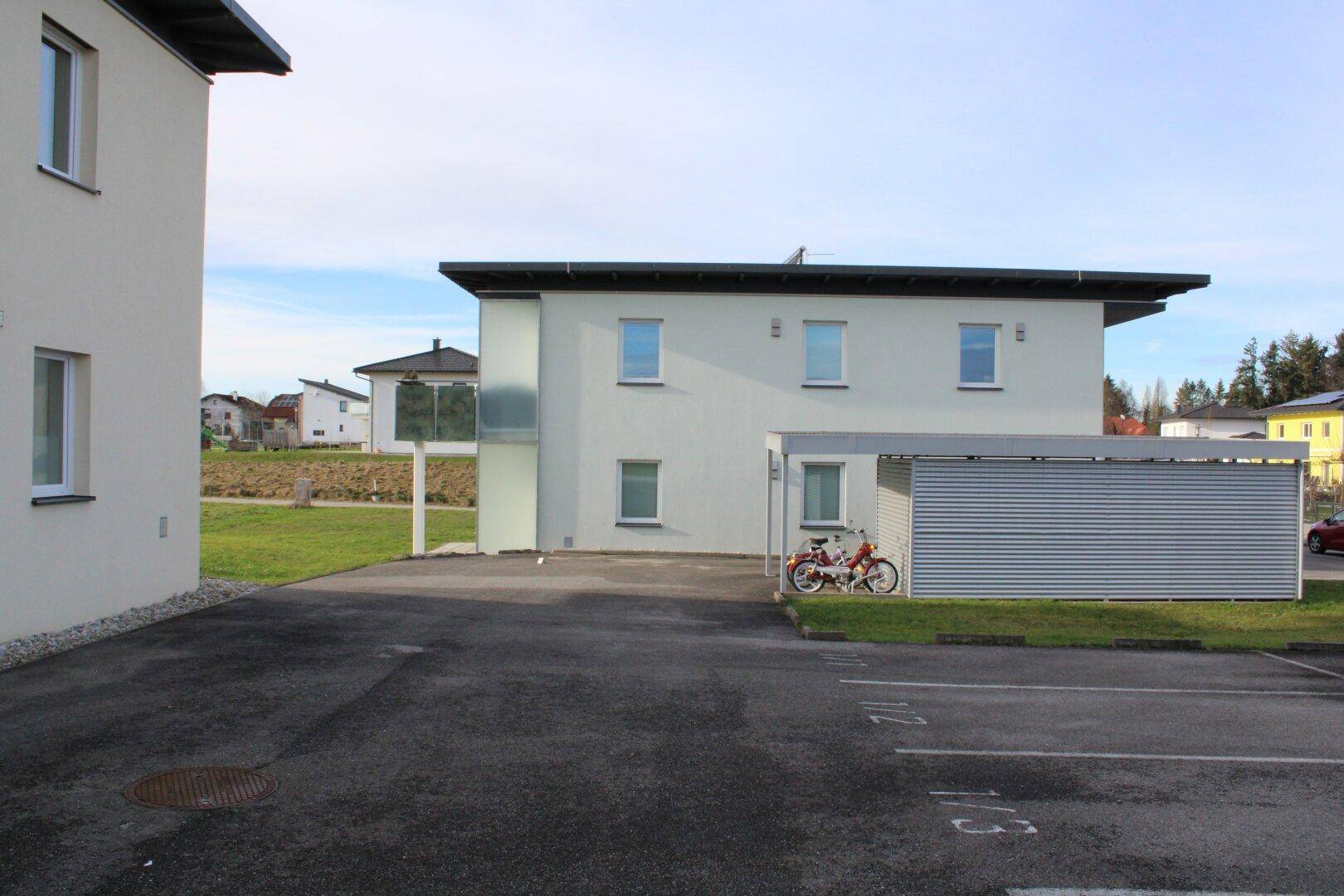 Moderne Gebäudeaußenansicht mit Parkplatz, Carport und Fahrradabstellplatz.