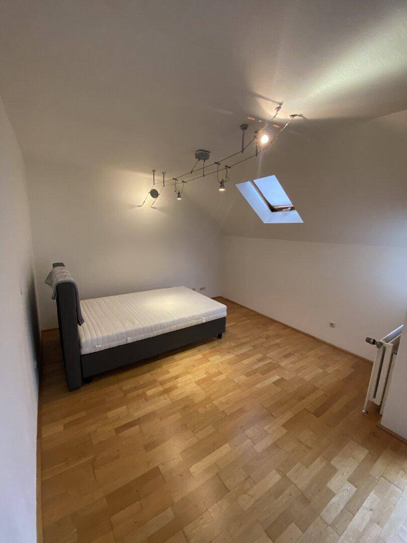 Helles Schlafzimmer im Dachgeschoss mit Holzboden, einem Bett und Dachfenster.
